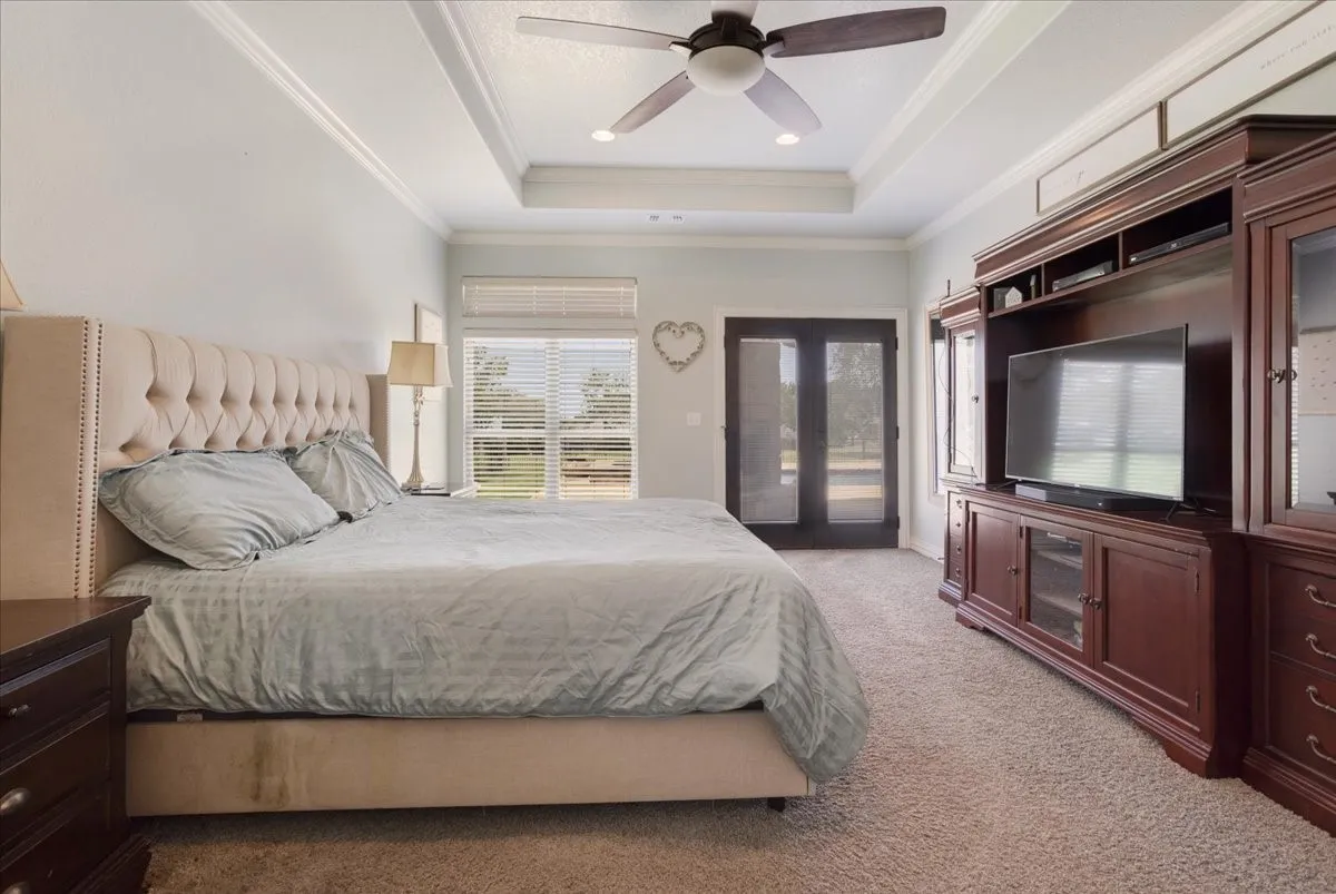 Tray ceiling with crown molding, ceiling fan, carpet flooring, windows with blinds, and double French doors