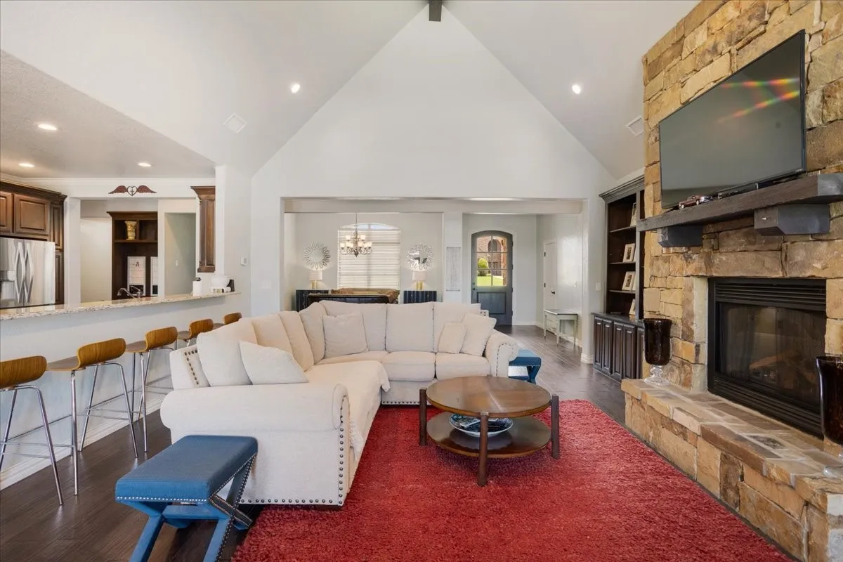 Vaulted ceiling with recessed lighting, stone-clad fireplace, wood-finish flooring, built-in shelving, and a breakfast bar with stone countertops
