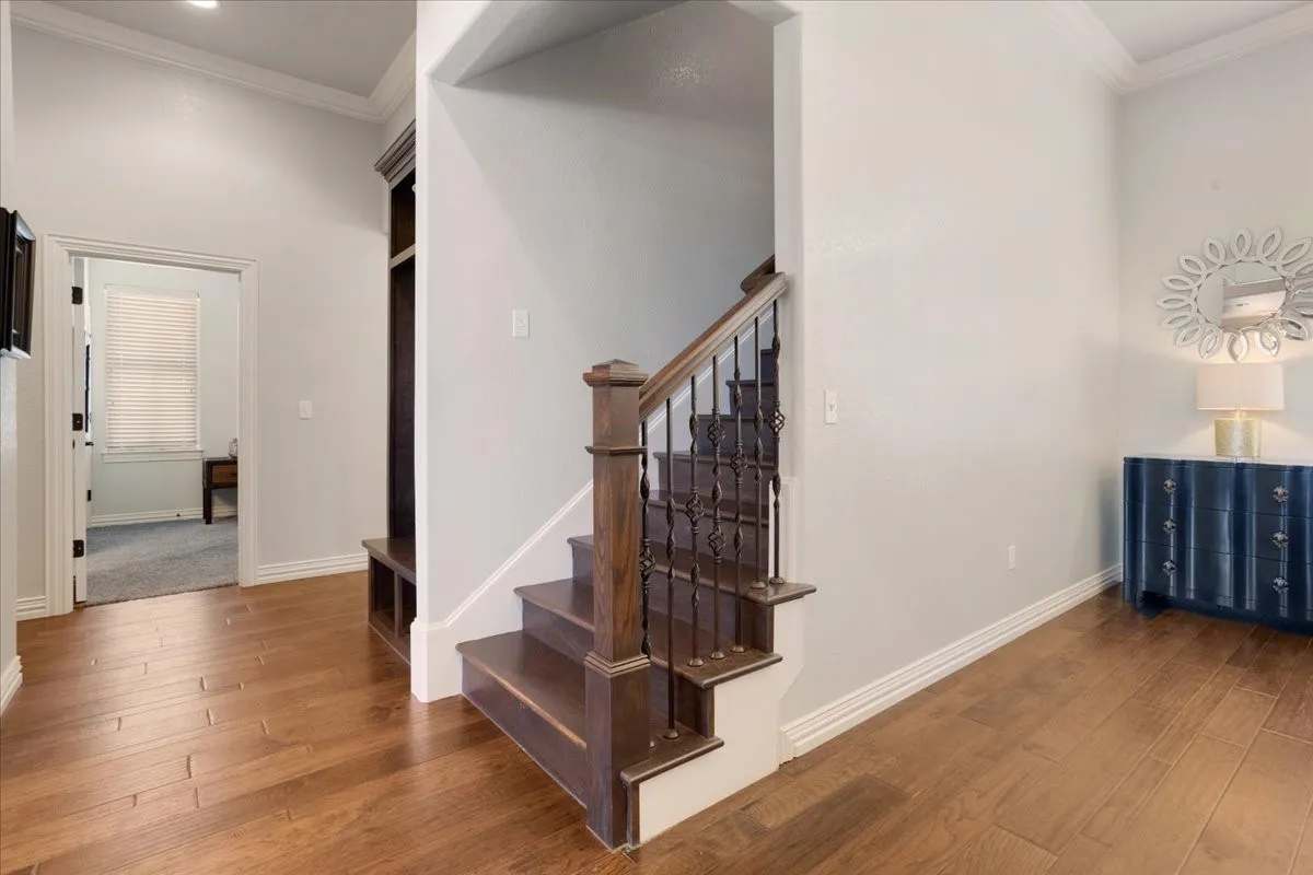 Wood-finish flooring, staircase with dark wood treads and wrought iron balusters, crown molding, built-in shelving, and recessed lighting
