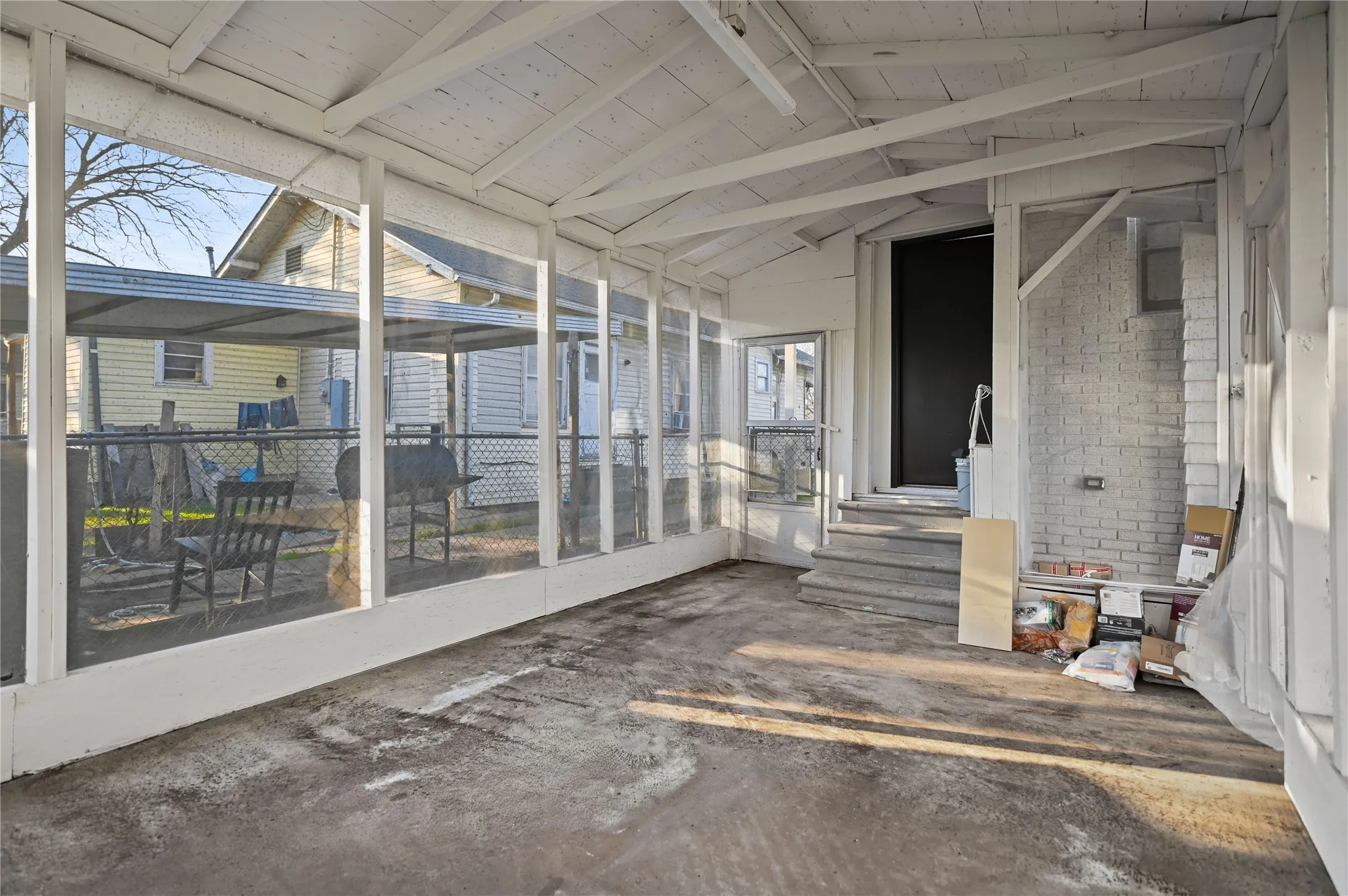 Screened porch with exposed rafter ceiling, concrete flooring, and painted brick wall