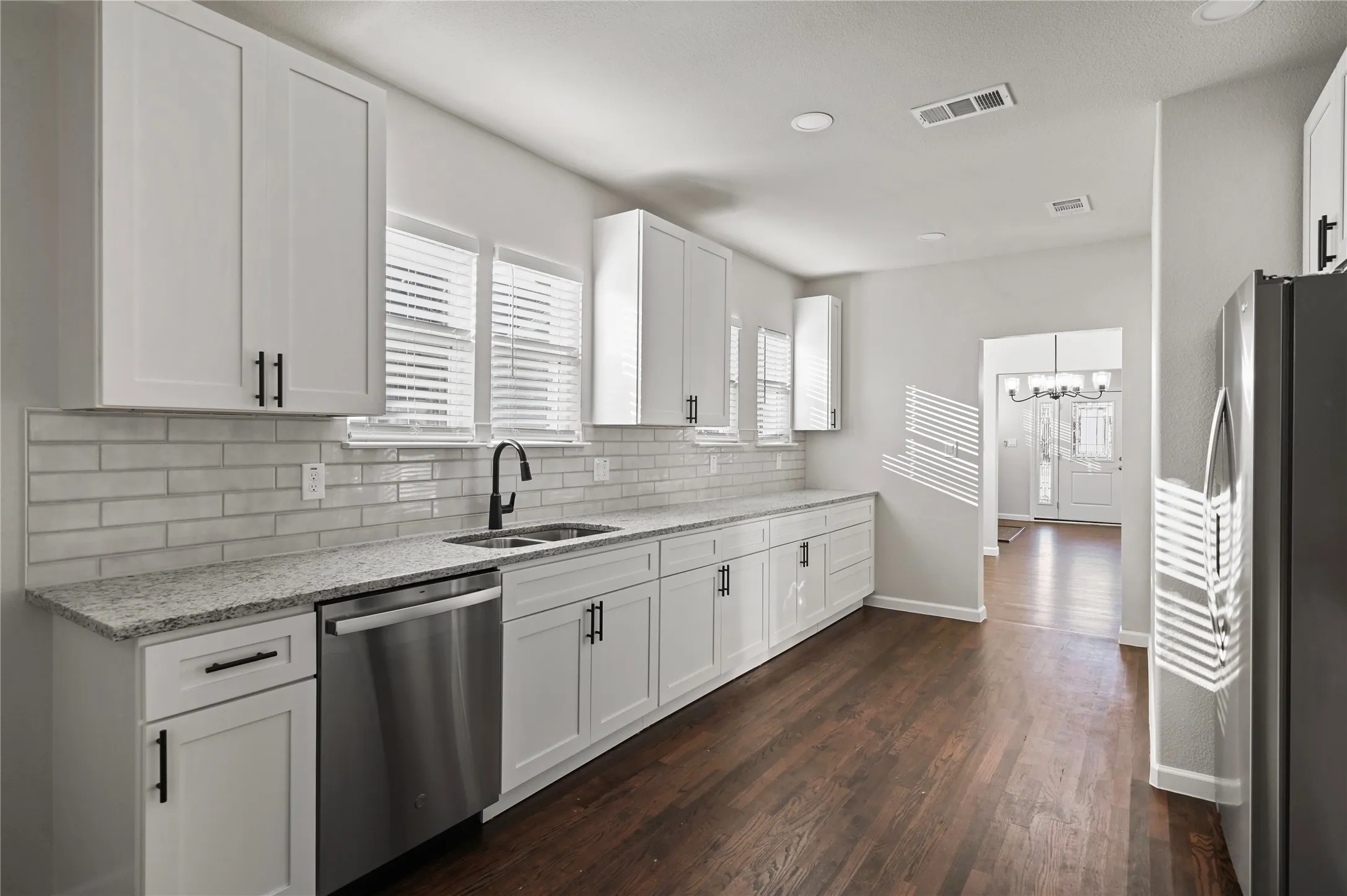 Kitchen featuring white shaker cabinetry, stainless steel appliances, light granite countertops, and a subway tile backsplash