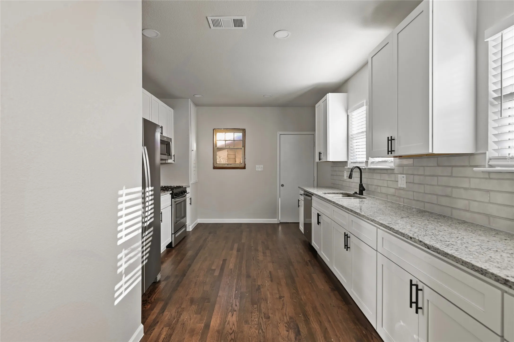Kitchen featuring white cabinetry, stainless steel appliances, wood-finish flooring, light-toned countertops, and a white subway tile backsplash