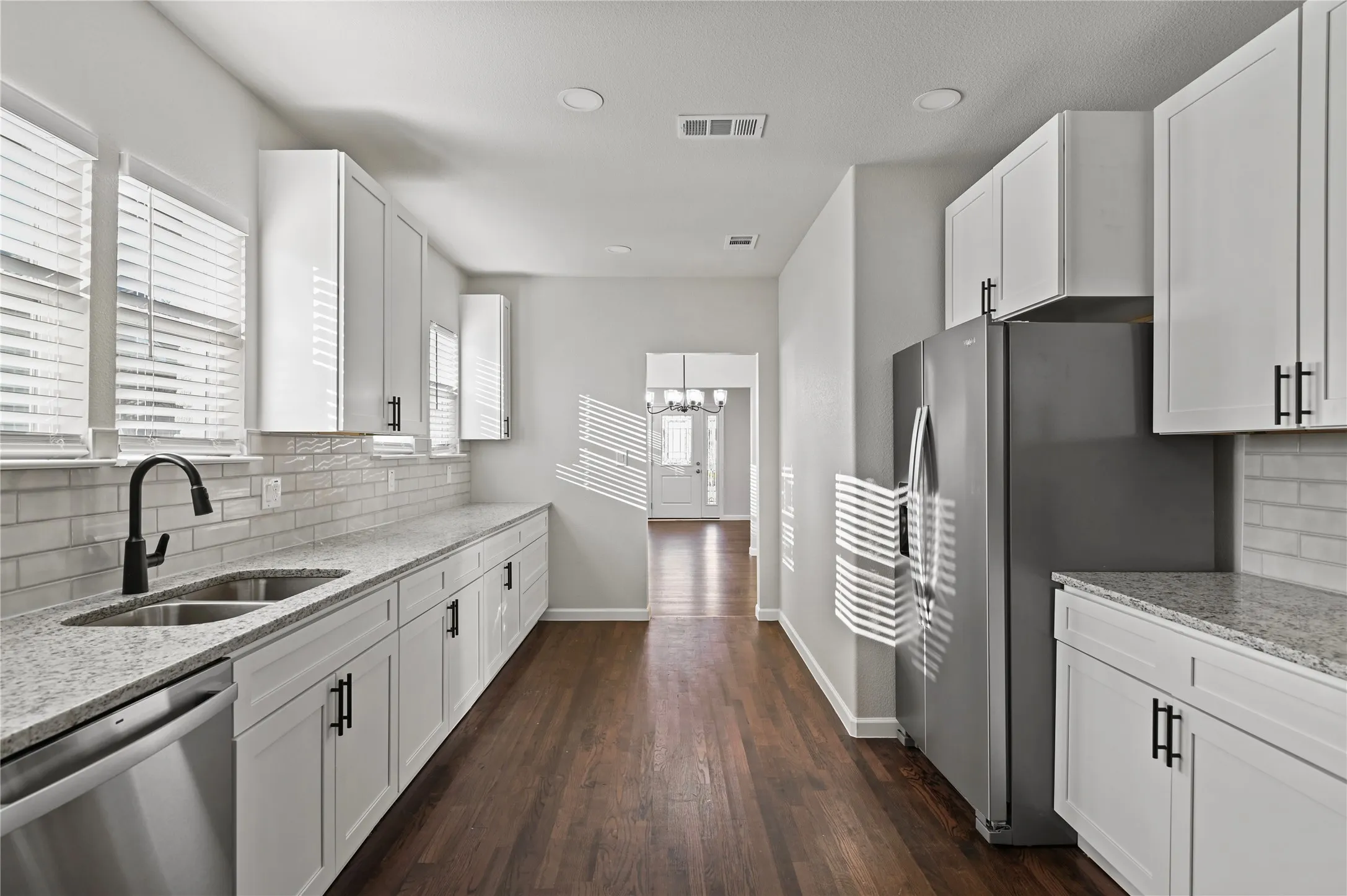 Galley kitchen featuring white cabinetry, stainless steel appliances, light-toned countertops, subway tile backsplash, and wood-finish flooring
