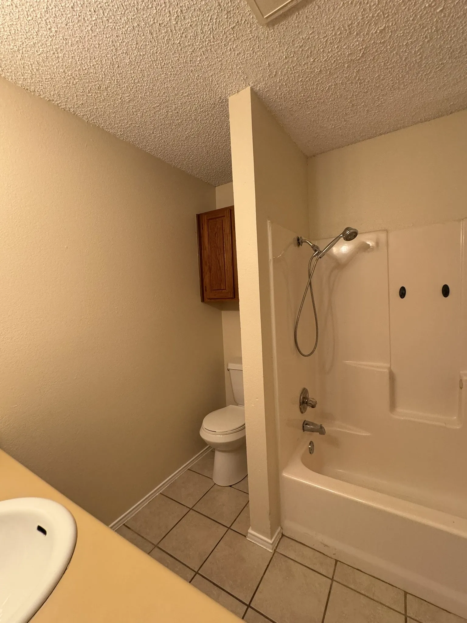 Bathroom featuring a built-in tub/shower combination with a showerhead, a toilet, a wall-mounted wood-finish cabinet, and tile flooring