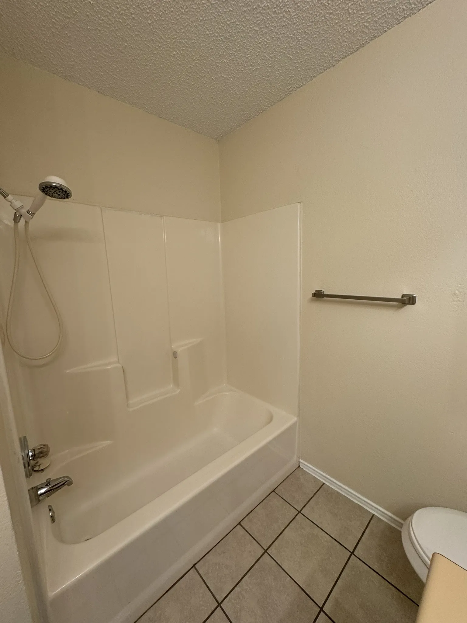 Tub and shower combination with a handheld showerhead, chrome fixtures, and tiled flooring