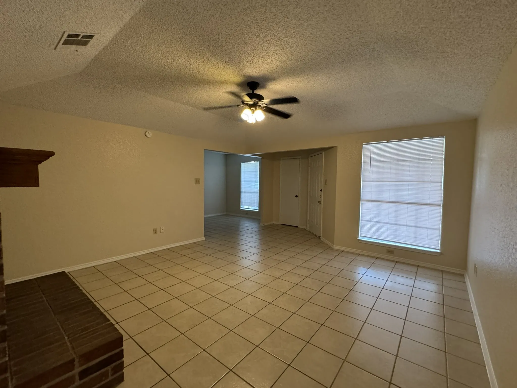 Tile flooring throughout, an overhead ceiling fan with lighting, a brick fireplace with a wood mantle, and window treatments