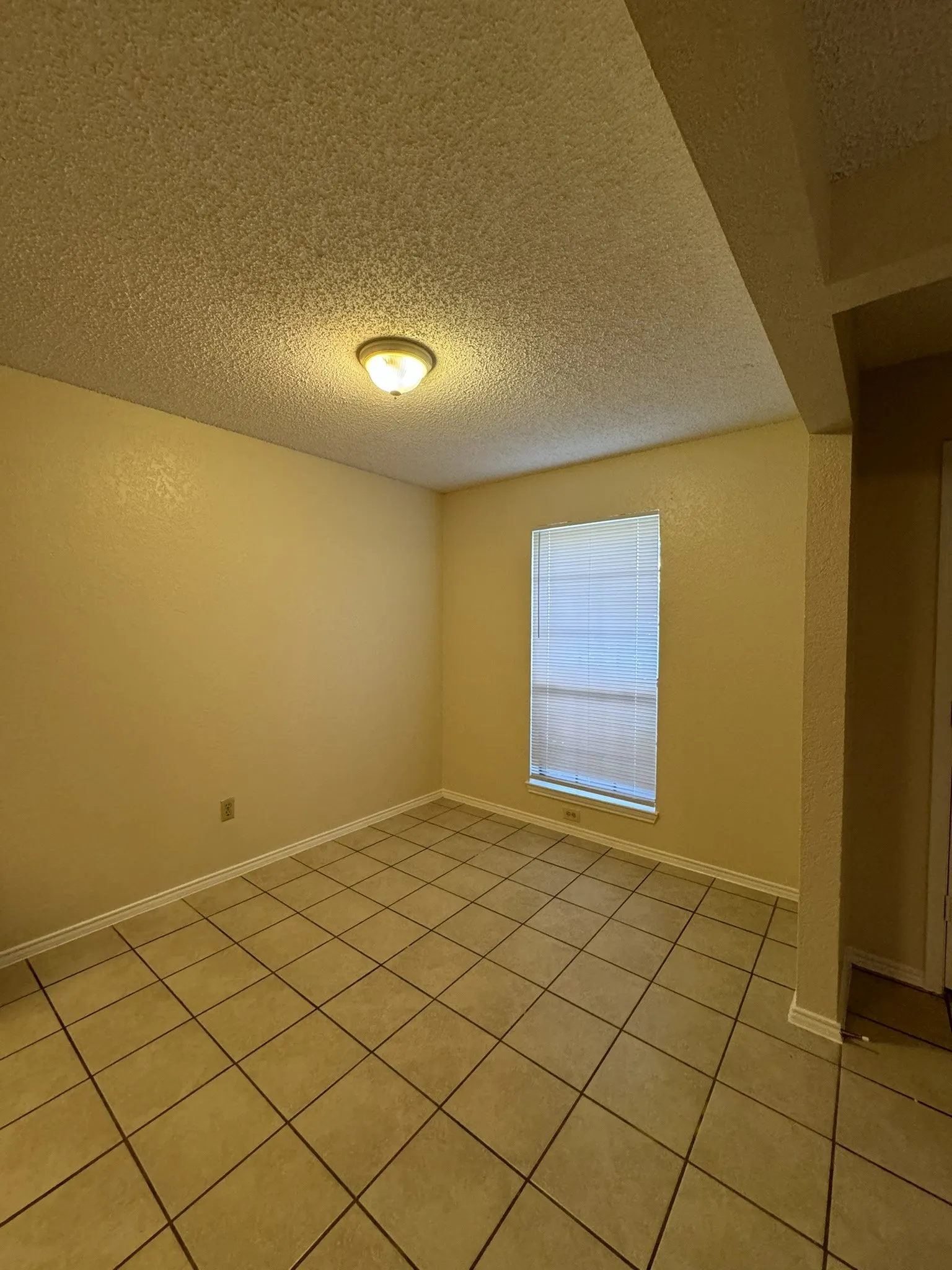 Recessed window with blinds, overhead flush mount lighting, textured ceilings, and neutral-toned ceramic tile flooring