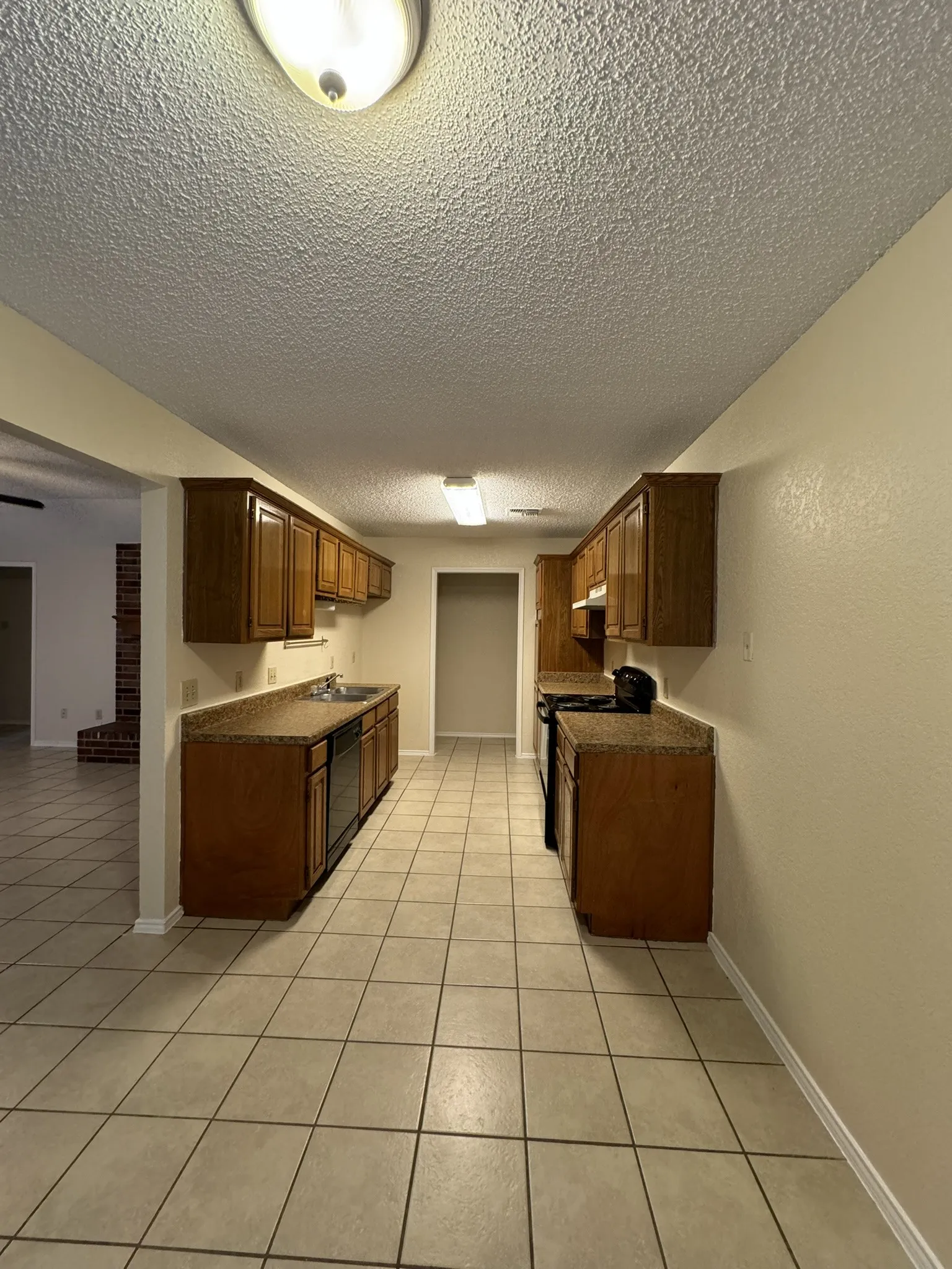Galley kitchen featuring tile flooring, wooden cabinetry, and durable countertops