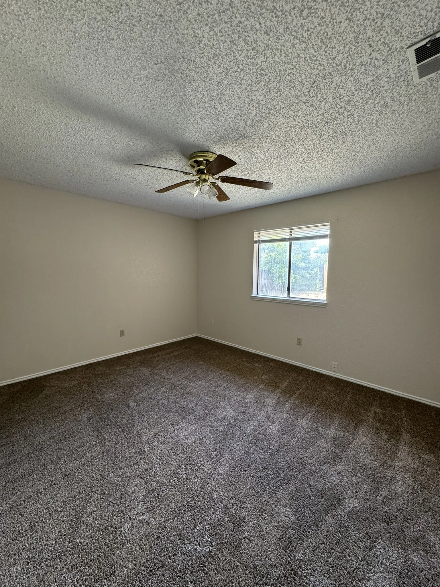 Neutral wall paint, textured ceiling, ceiling fan with integrated lighting, window with natural light, and plush carpet flooring