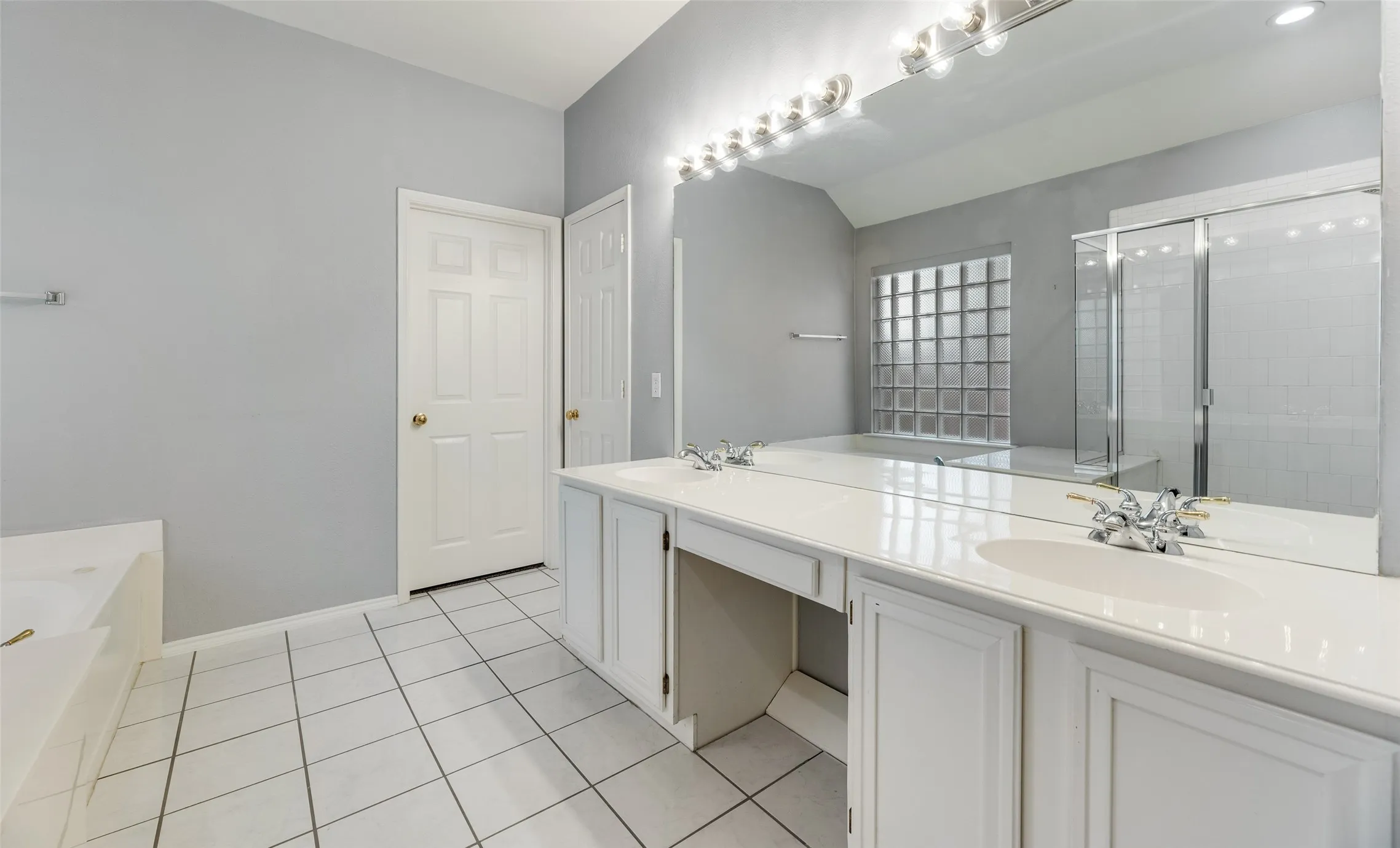 Dual vanity with integrated sinks, expansive mirror, tile flooring, glass block window, and a shower enclosure