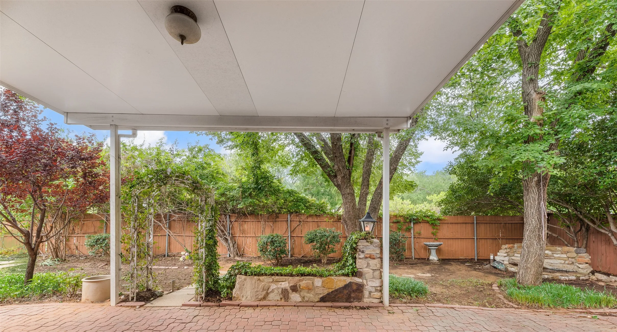 Covered patio featuring a brick paver surface, stone-clad planter, and a garden arbor