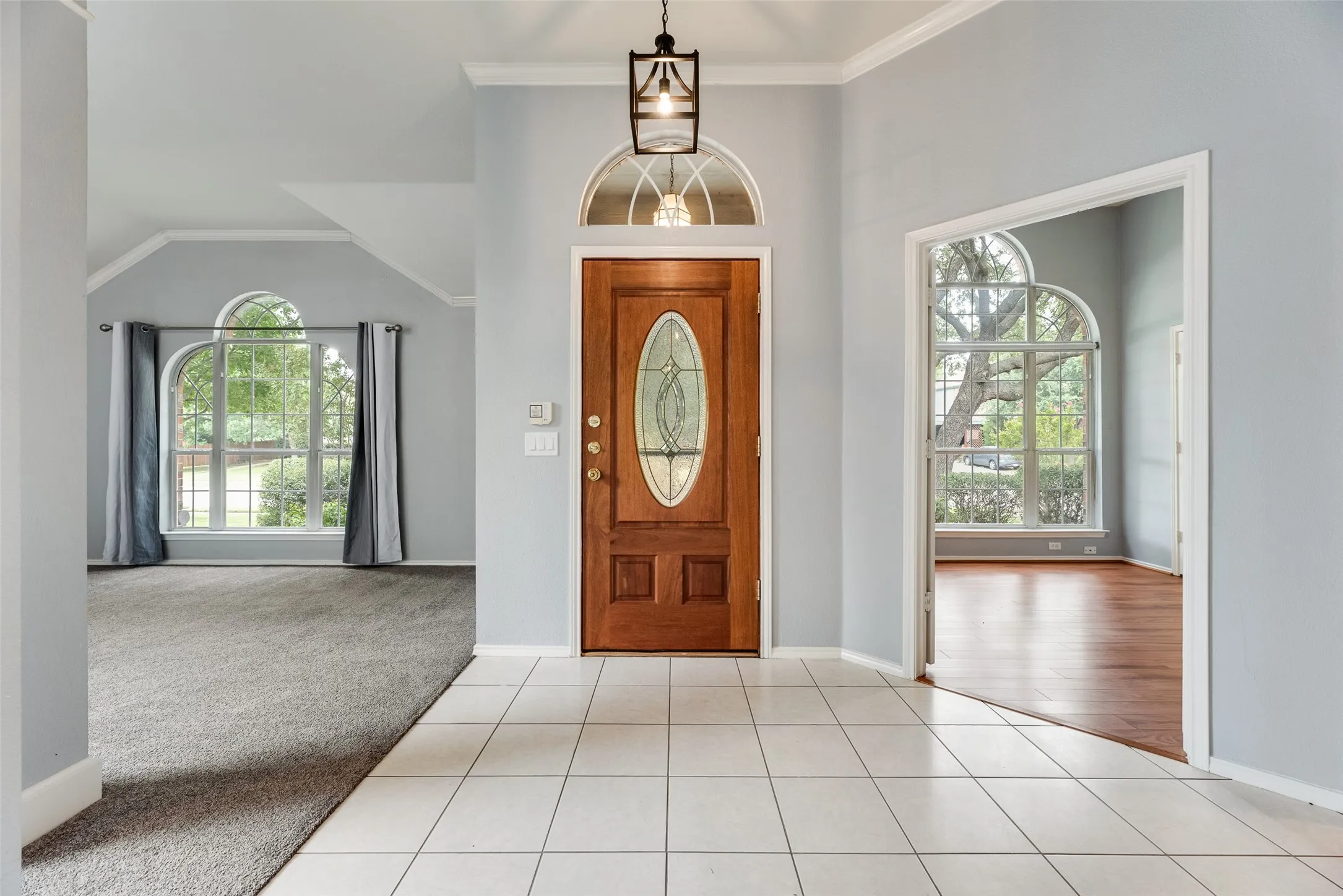 Entryway featuring tile flooring, a wood-finish front door with an oval glass insert, and an arched transom window