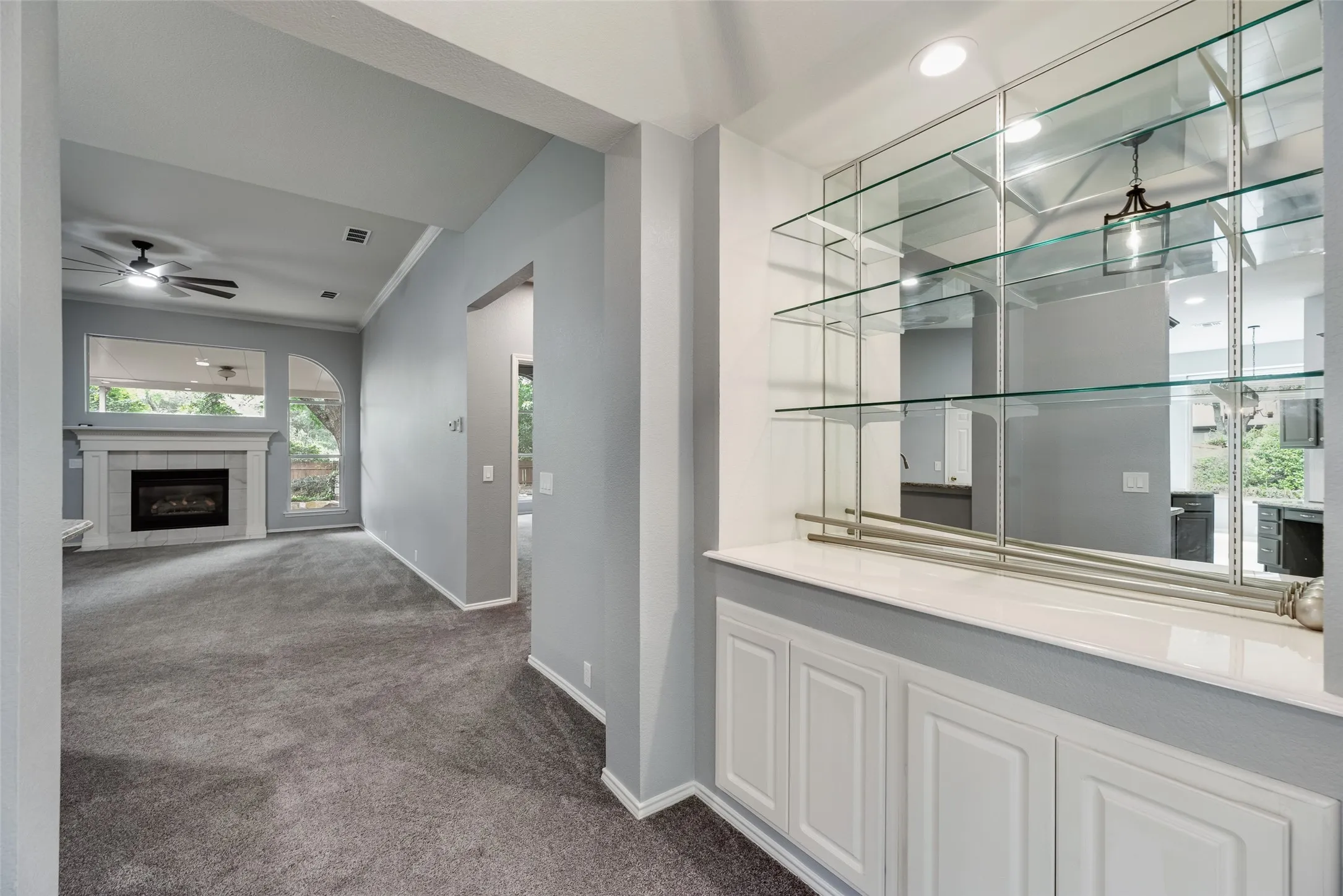 Built-in wet bar with glass shelving and lower cabinetry, fireplace with a mantle, and a ceiling fan