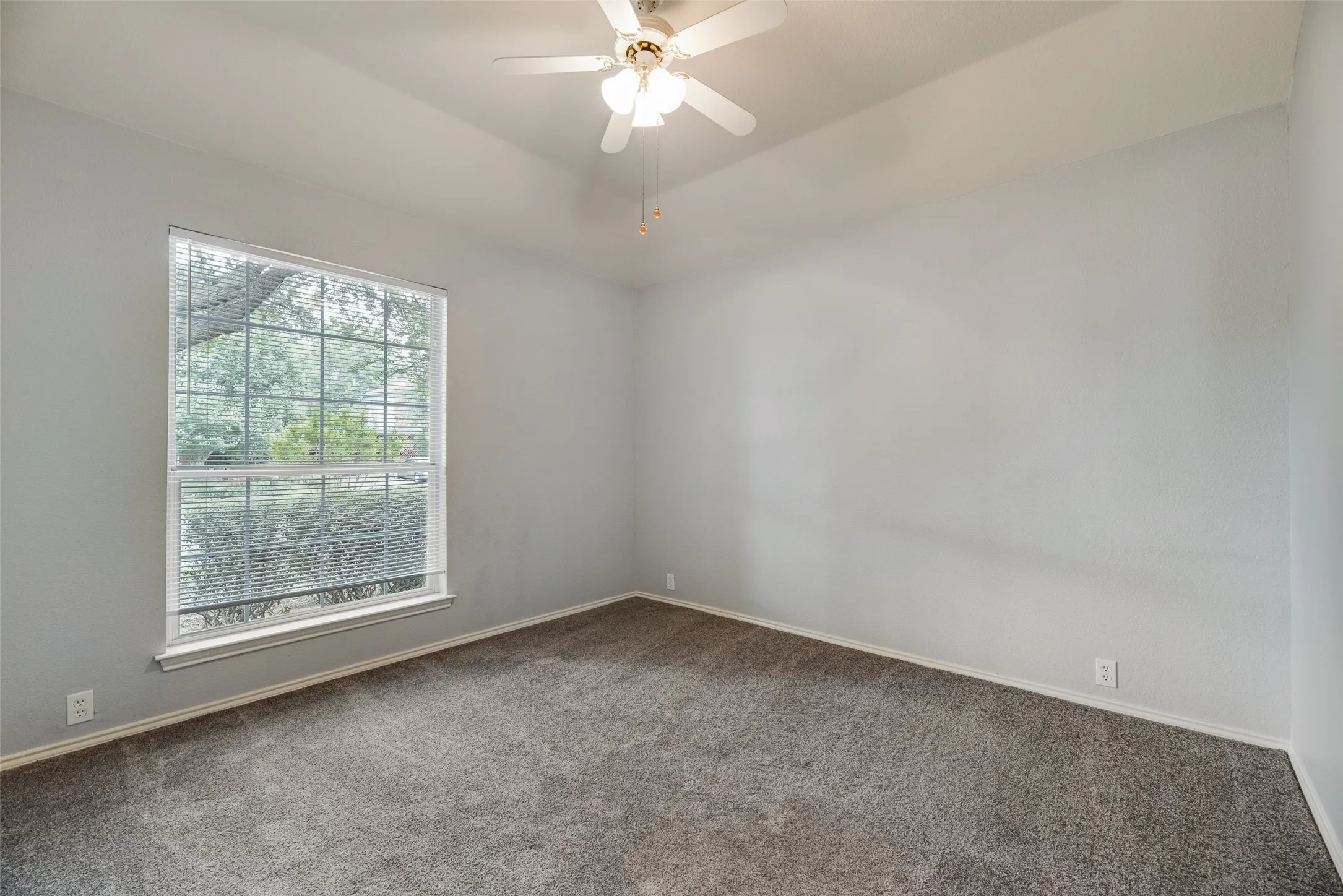 Carpeted flooring, vaulted ceiling, ceiling fan with light fixture, window with blinds, and neutral wall paint