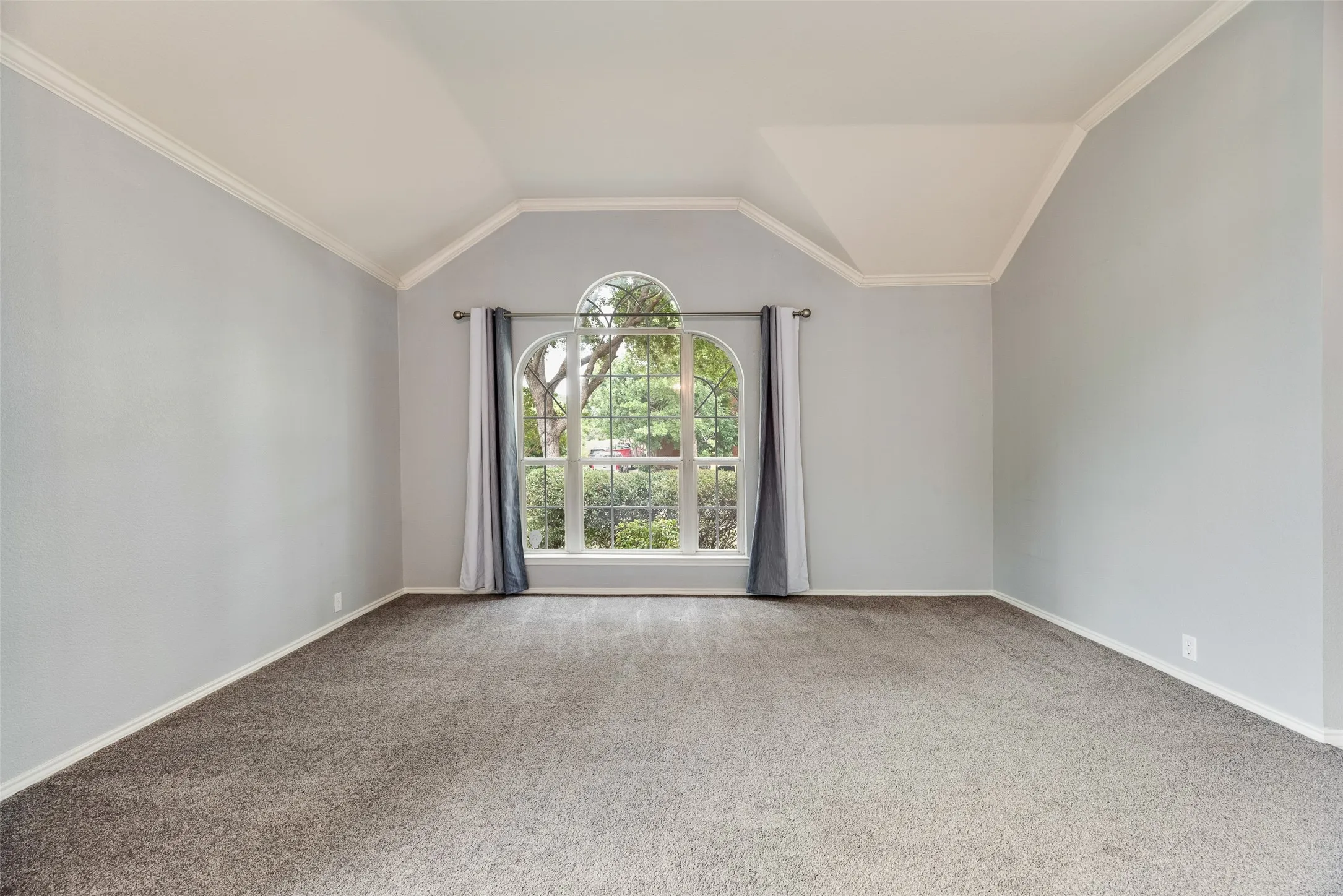 Vaulted ceiling with crown molding, arched window, and neutral wall tones