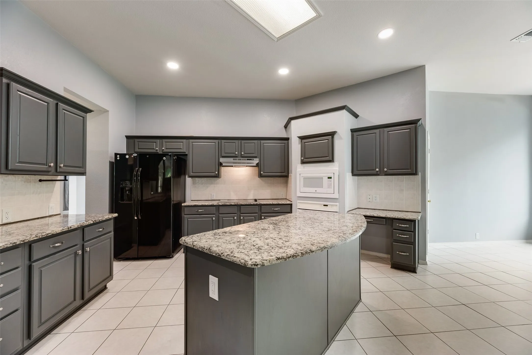 Kitchen featuring dark cabinetry, light-toned countertops, a built-in microwave, tile flooring, and recessed lighting