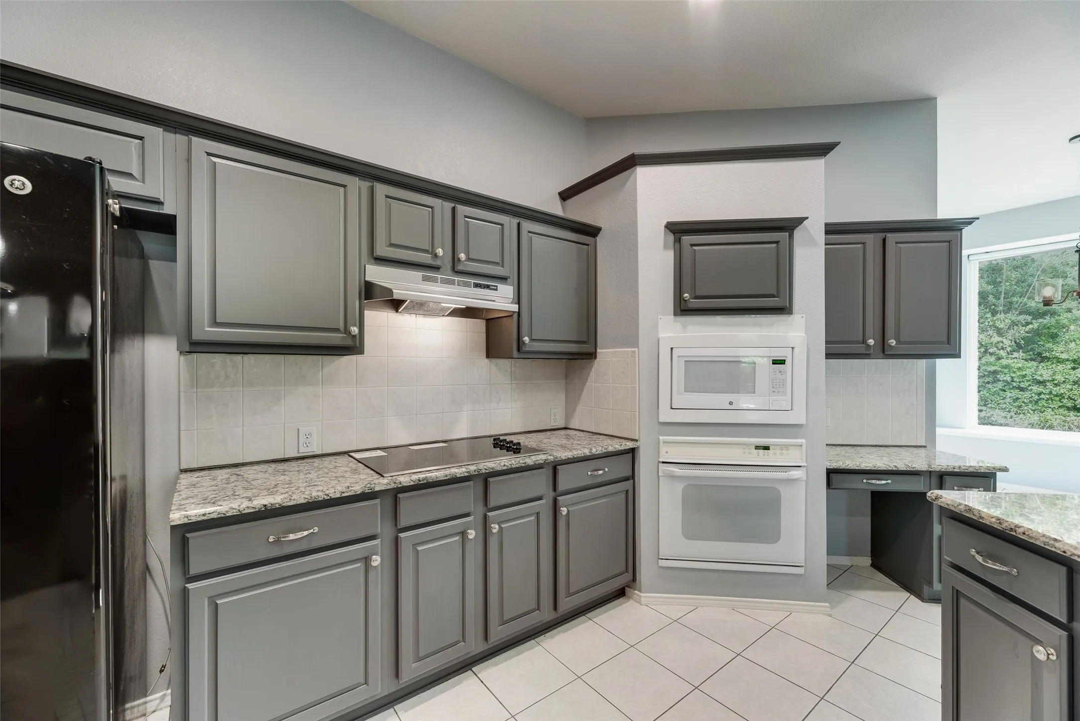 Kitchen featuring gray shaker-style cabinetry, light-toned tile backsplash, and speckled countertops
