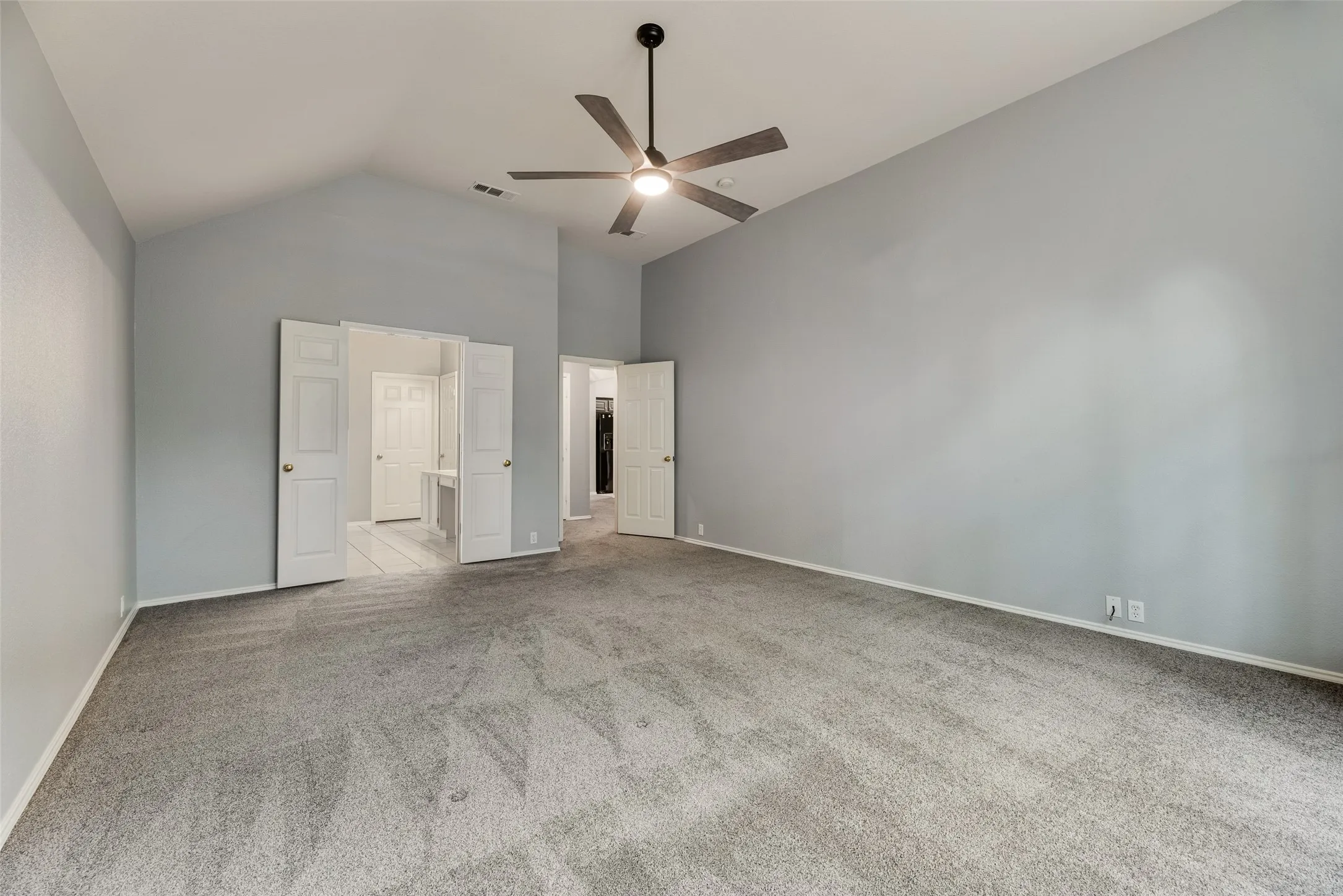 Vaulted ceiling with an attached ceiling fan, neutral wall paint, and gray carpet flooring