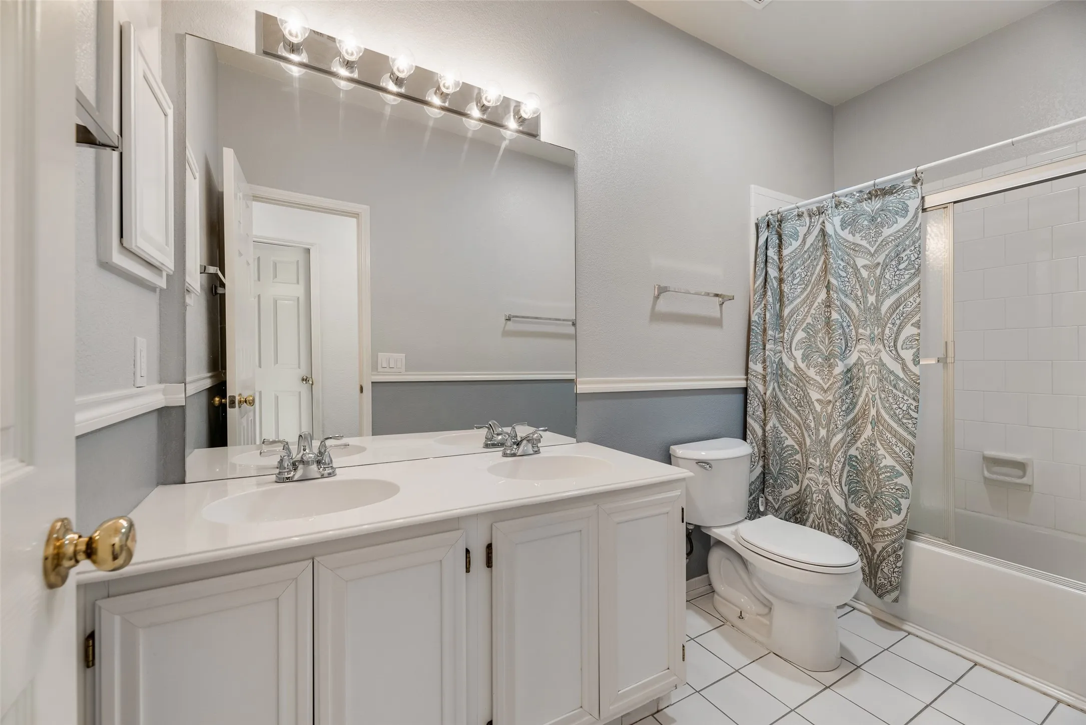 Dual vanity with integrated sinks, expansive wall-mounted mirror, overhead vanity lighting, white tile flooring, and a shower-tub combination with white subway tile surround