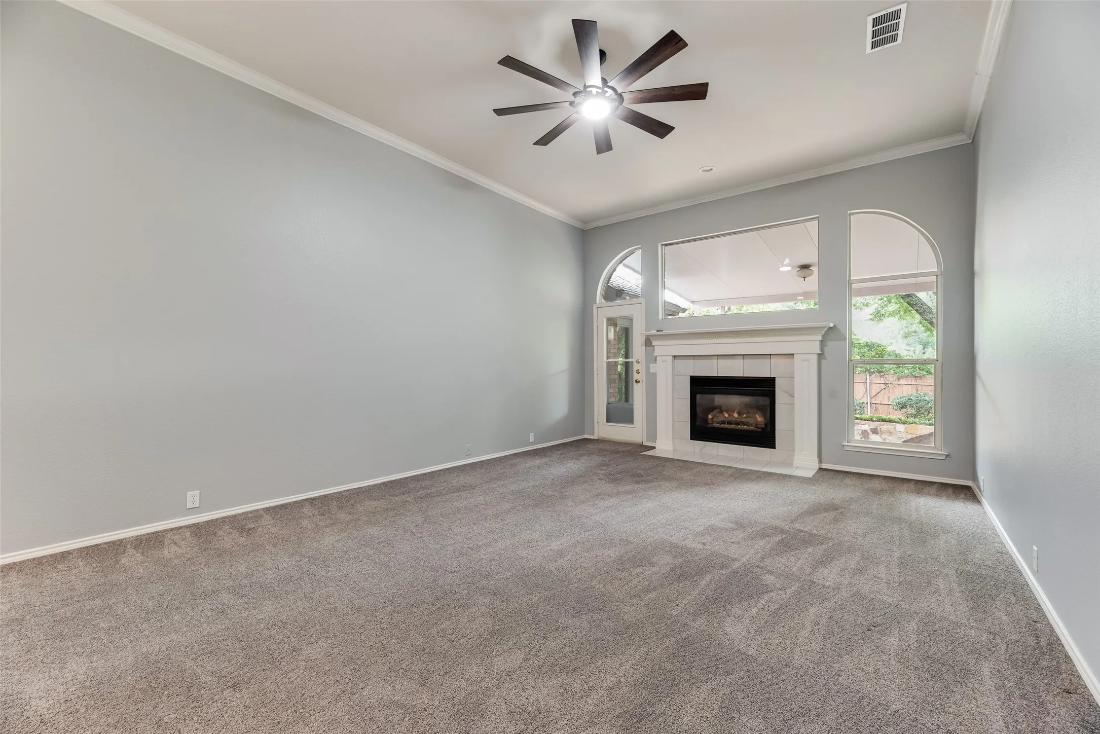 Vaulted ceiling with an attached ceiling fan, floor-to-ceiling fireplace with a tile surround, and arched window details