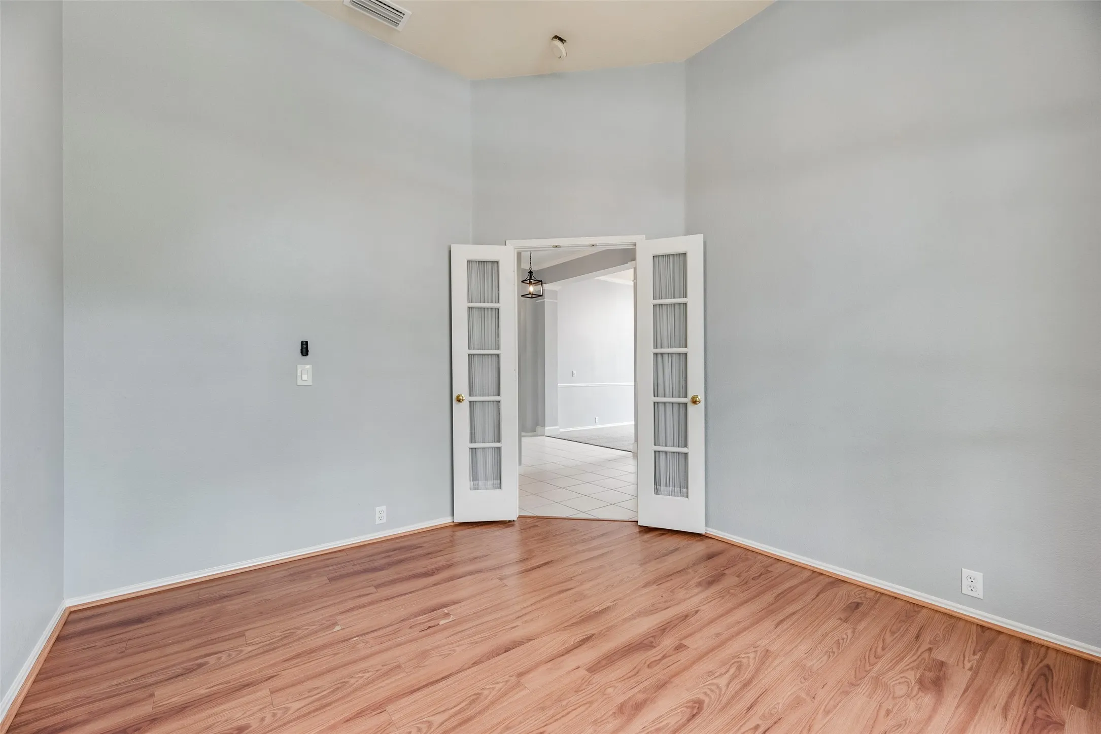 Wood-finish flooring with light gray walls, featuring double French doors with frosted glass panels, and a vaulted ceiling