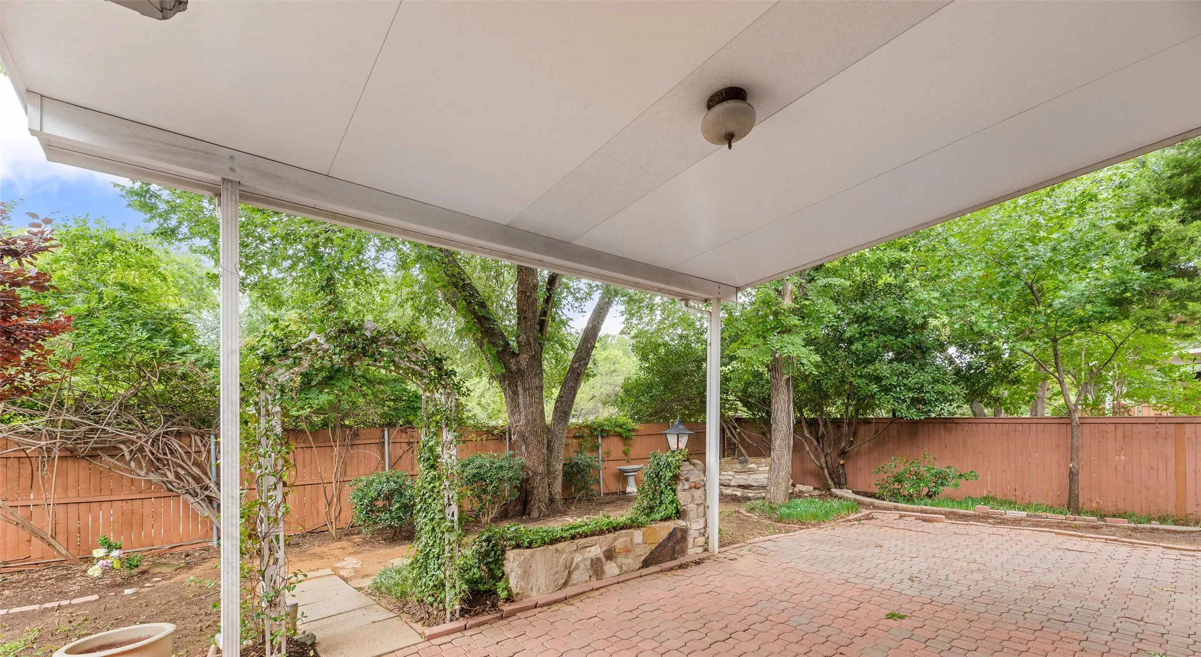 Covered patio with a paver surface, bordered by a wooden fence
