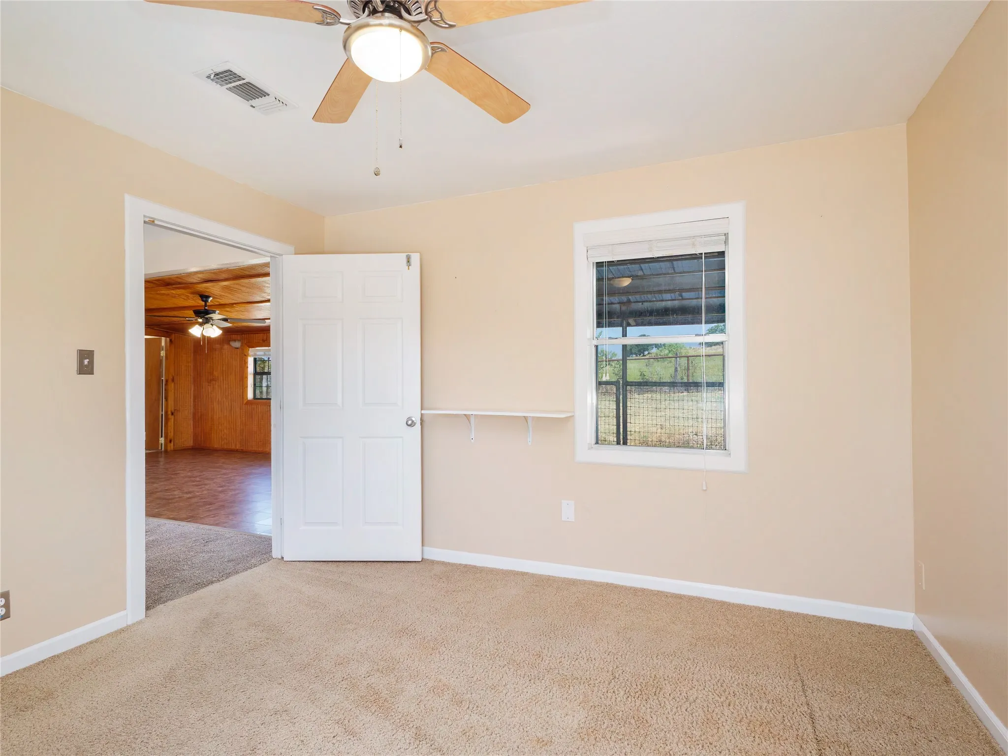 Neutral tone wall paint, carpet flooring, a window with blinds, and a built-in ceiling fan