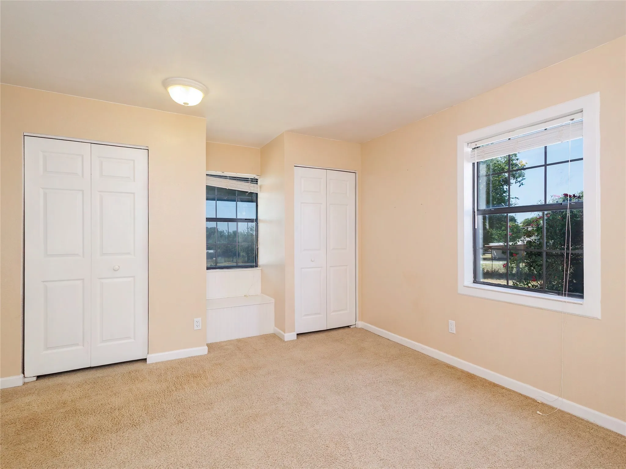 Wall-to-wall carpeting, two bi-fold door closets, recessed window featuring a built-in bench, and a ceiling-mounted light fixture