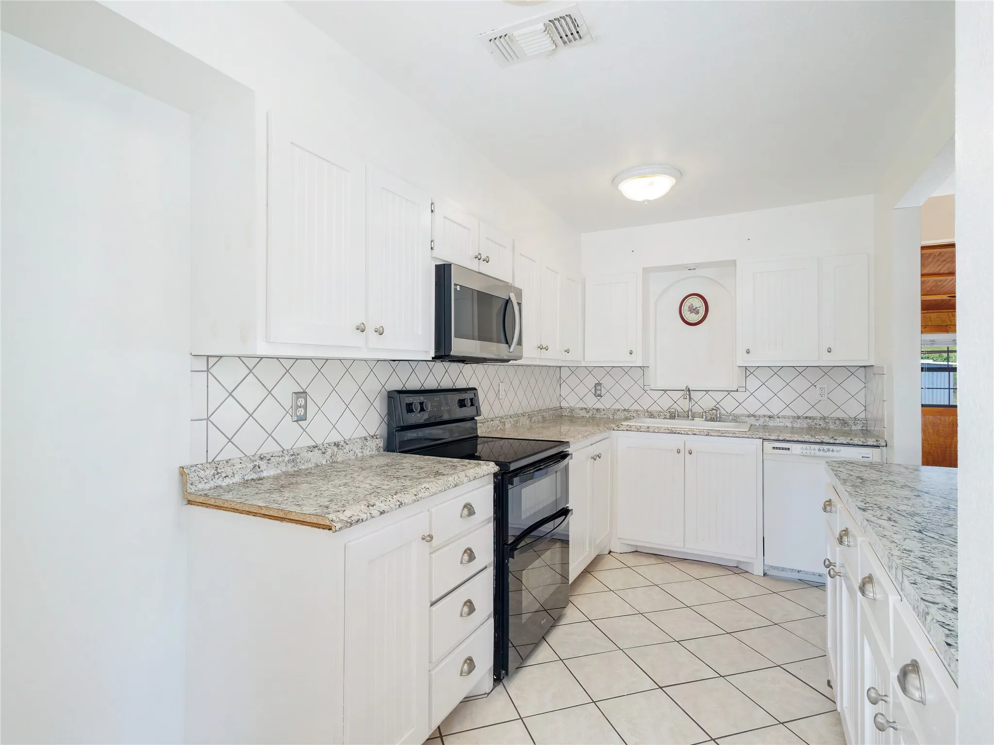 White cabinetry with beadboard accents, granite-style countertops, stainless steel microwave, black electric range, and diamond-pattern tile backsplash