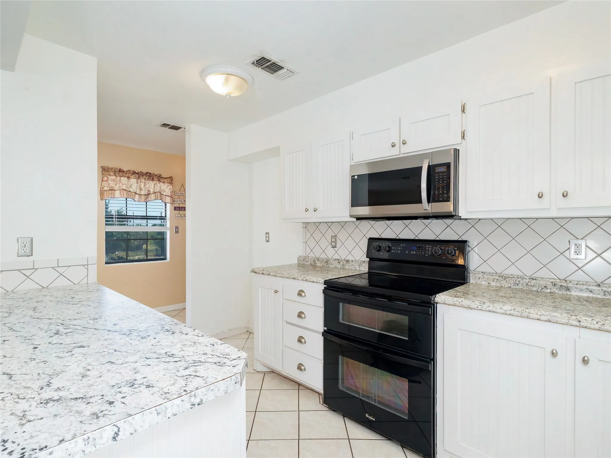 White cabinetry, stainless steel microwave, black double oven, tile flooring, and patterned tile backsplash