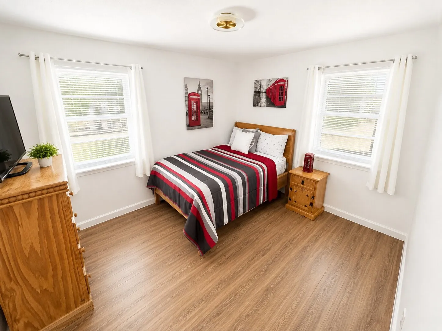 Wood-finish flooring, white walls, two windows with blinds, and a flush mount ceiling light fixture