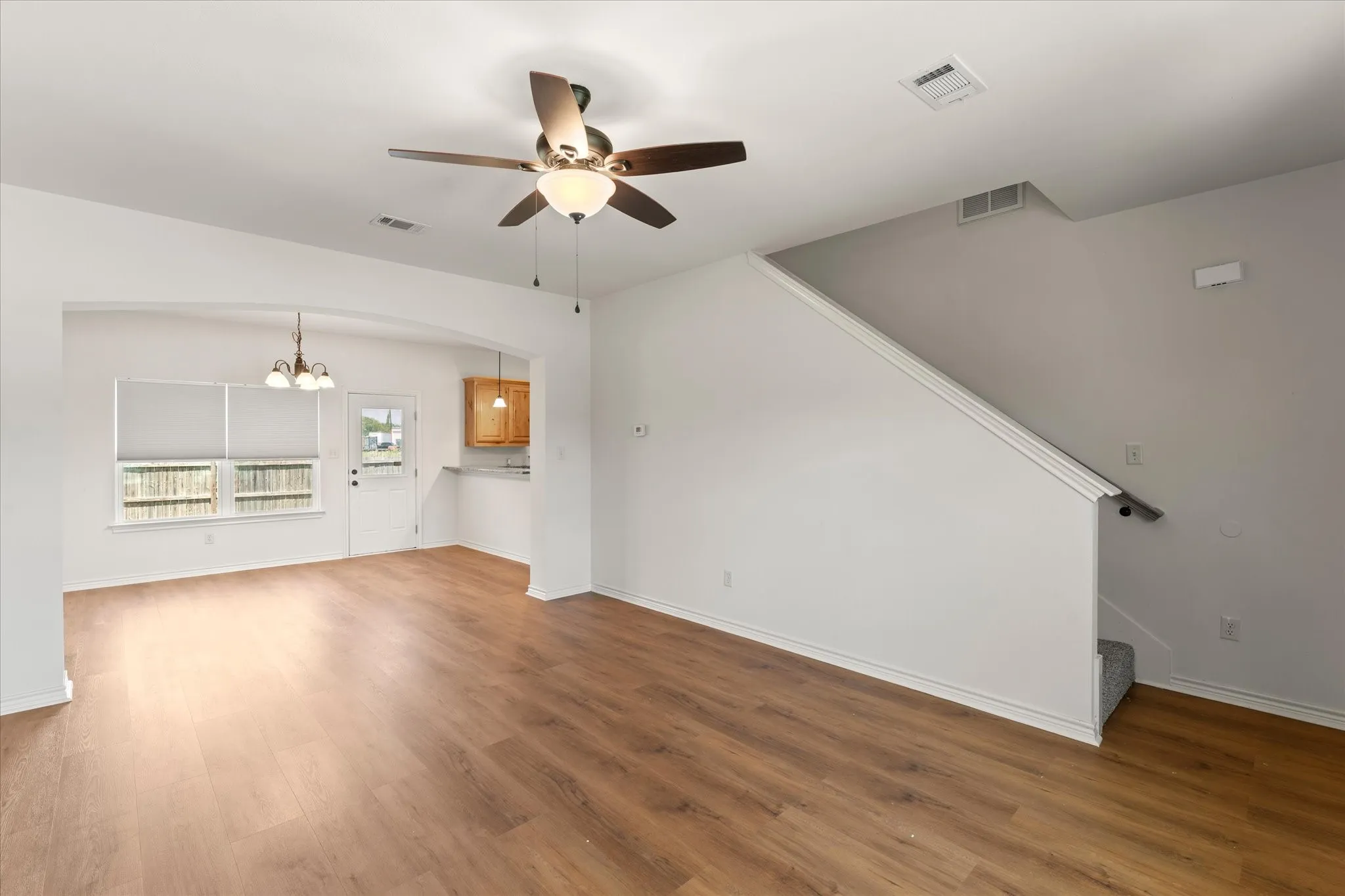 Spacious open-concept room featuring wood-finish flooring, an arched doorway, and a ceiling fan with integrated lighting
