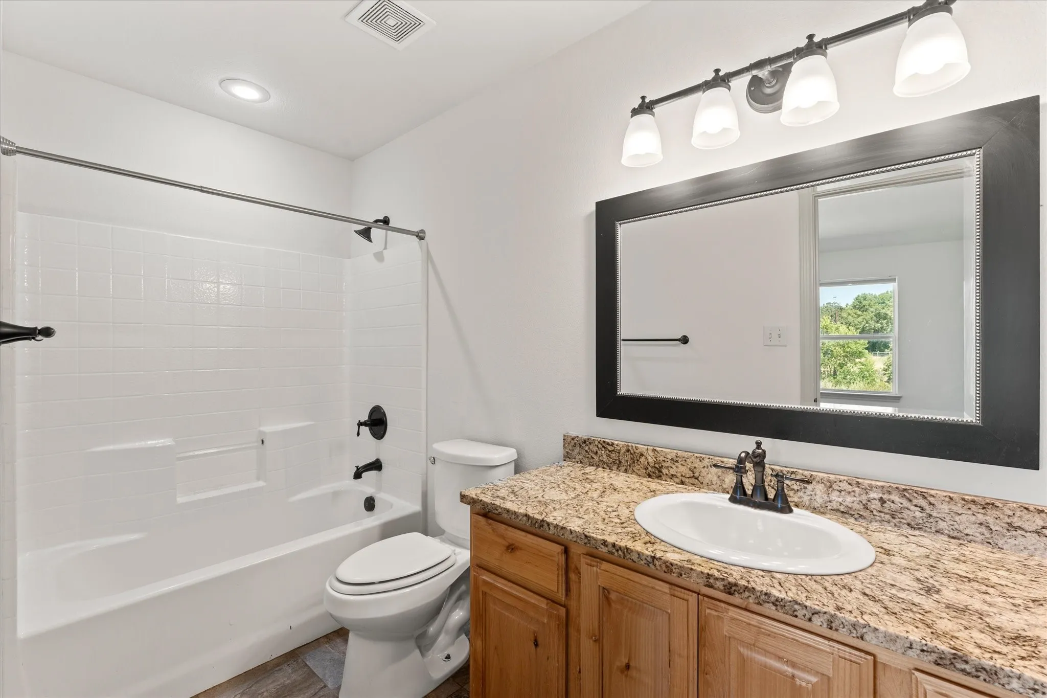 Full bathroom with a tub/shower combination, toilet, and vanity featuring a granite-finish countertop, undermount sink, and wood-finish cabinetry