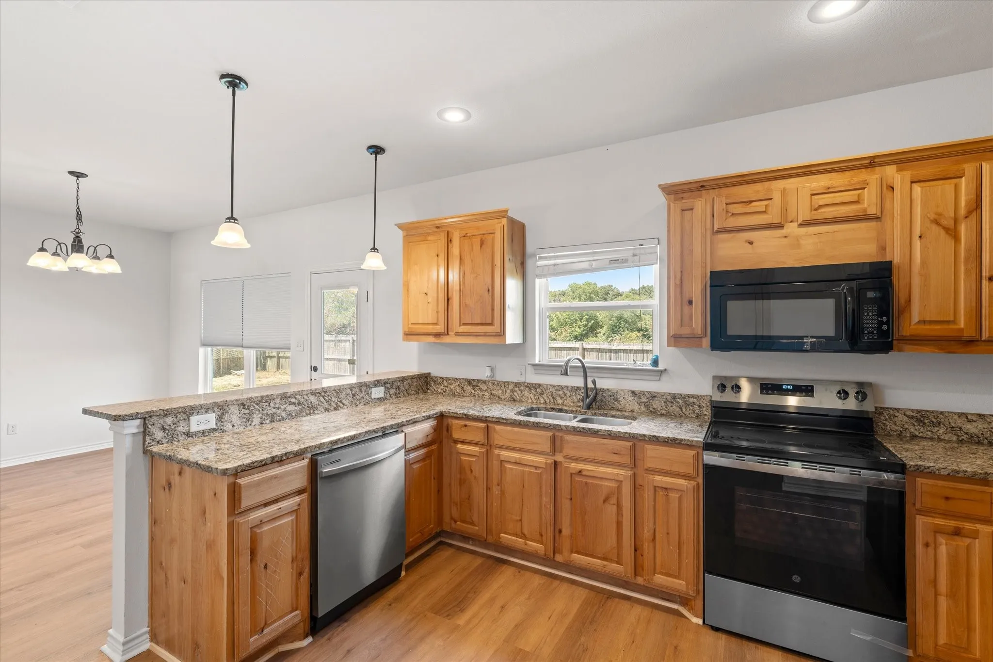 Kitchen featuring wood-finish cabinetry, granite countertops, stainless steel dishwasher, and built-in microwave