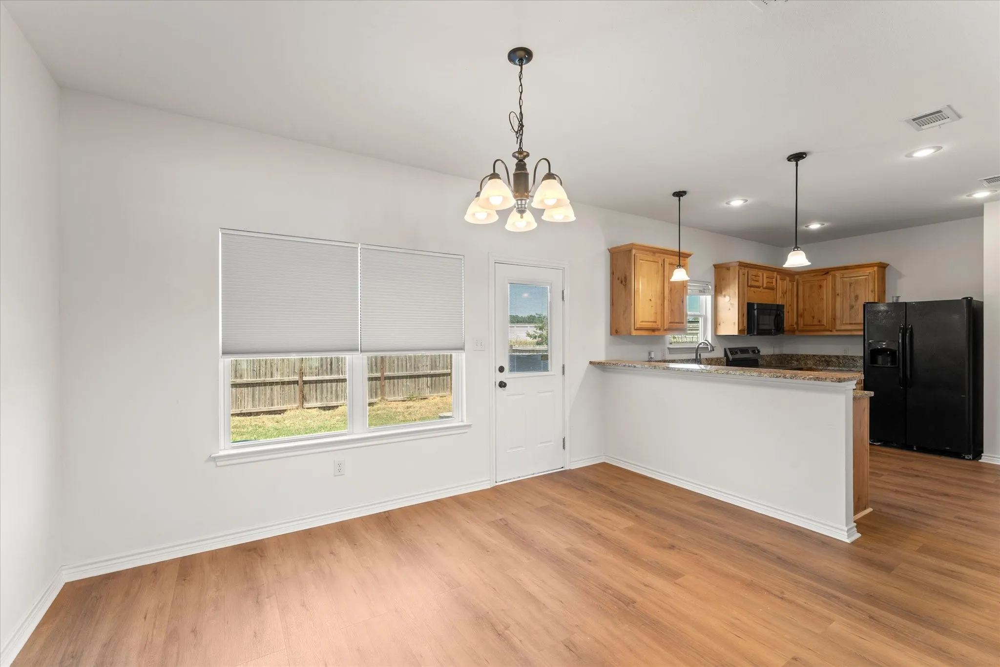 Open-concept living space with wood-finish flooring, kitchen featuring wood cabinetry, black appliances, and a breakfast bar