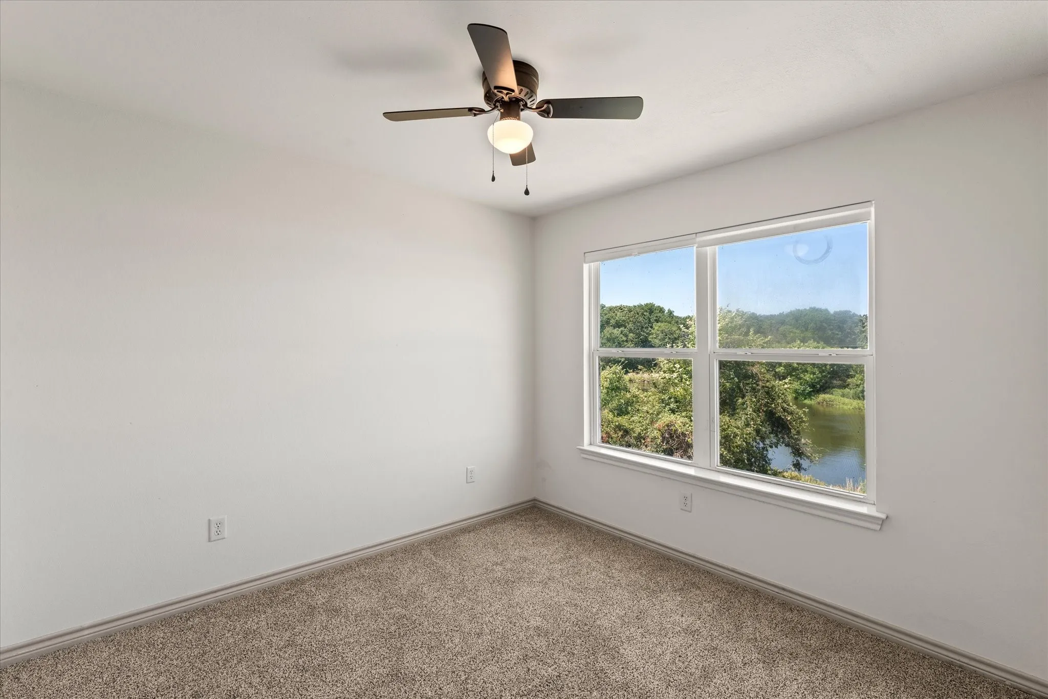 White walls with carpet flooring, featuring a ceiling fan with light fixture and a window with a natural landscape backdrop