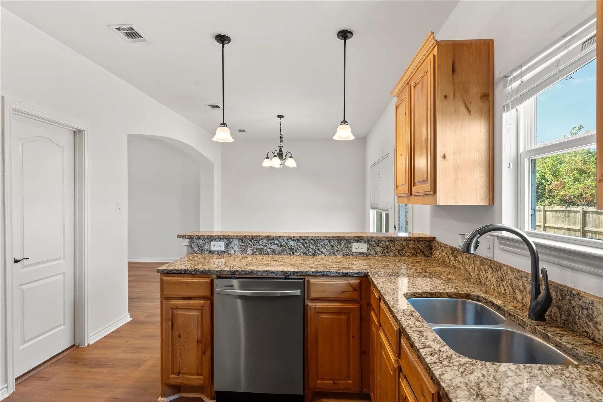 Kitchen featuring wood-finish cabinetry, granite countertops, a double basin stainless steel sink with a gooseneck faucet, and stainless steel appliances
