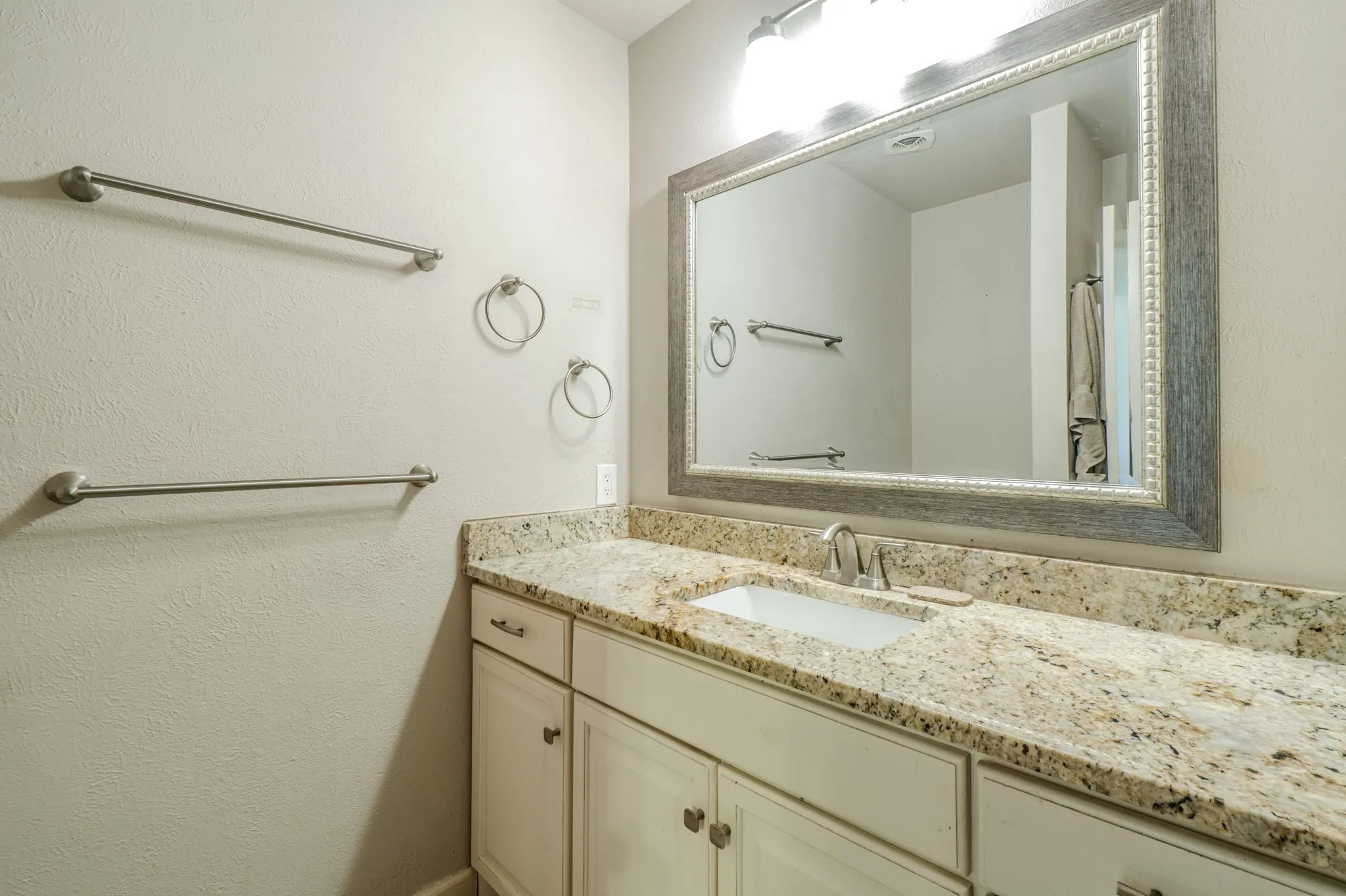 White vanity with multiple storage cabinets, an undermount sink, and a speckled countertop