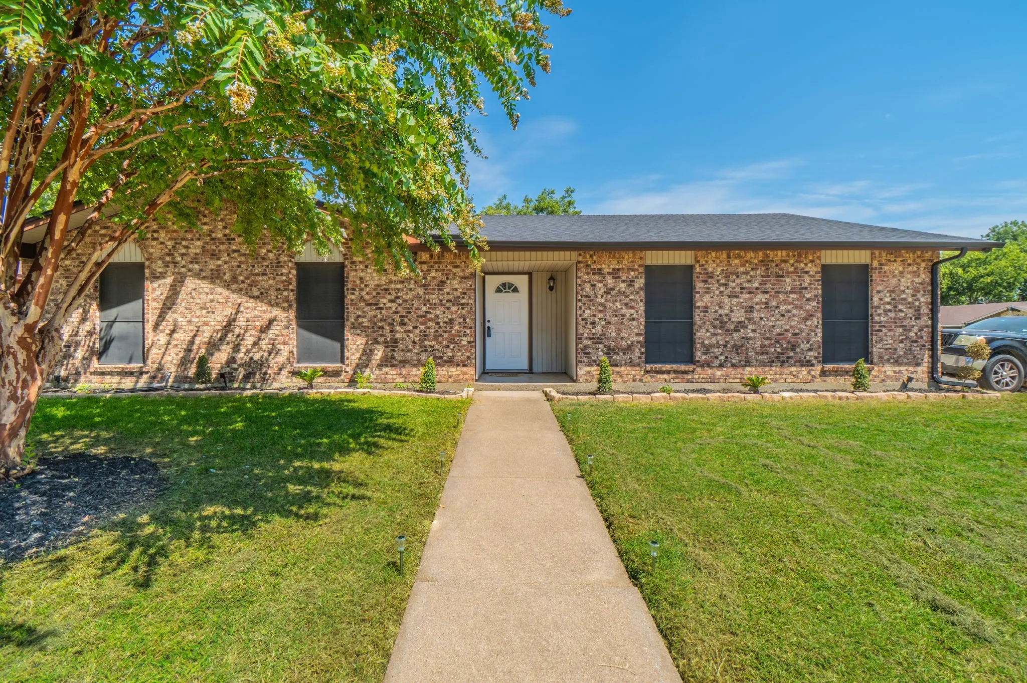 Brick facade featuring a white entry door, dark roof, and concrete pathway