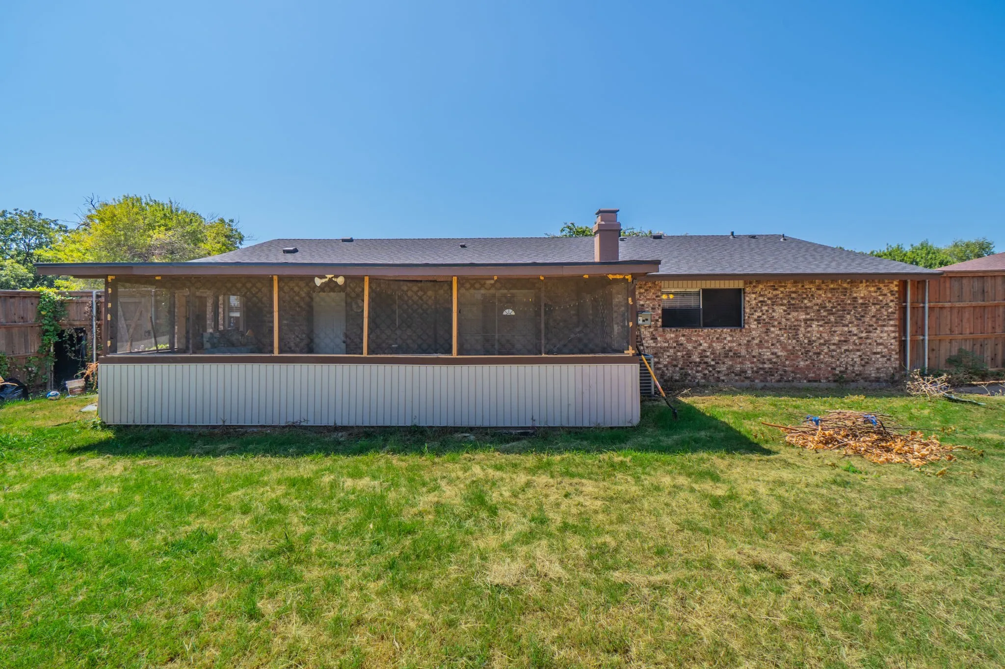 Expansive backyard featuring a screened-in porch with a wood frame, brick exterior, and wood fencing