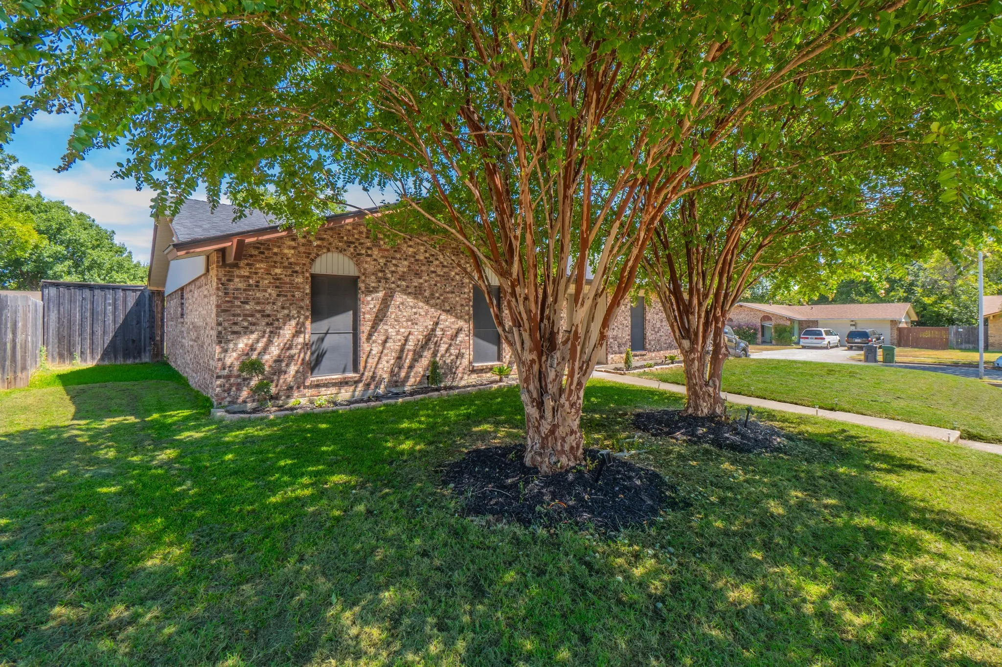 Brick exterior, arched window details, mature trees, manicured lawn, and a wooden privacy fence