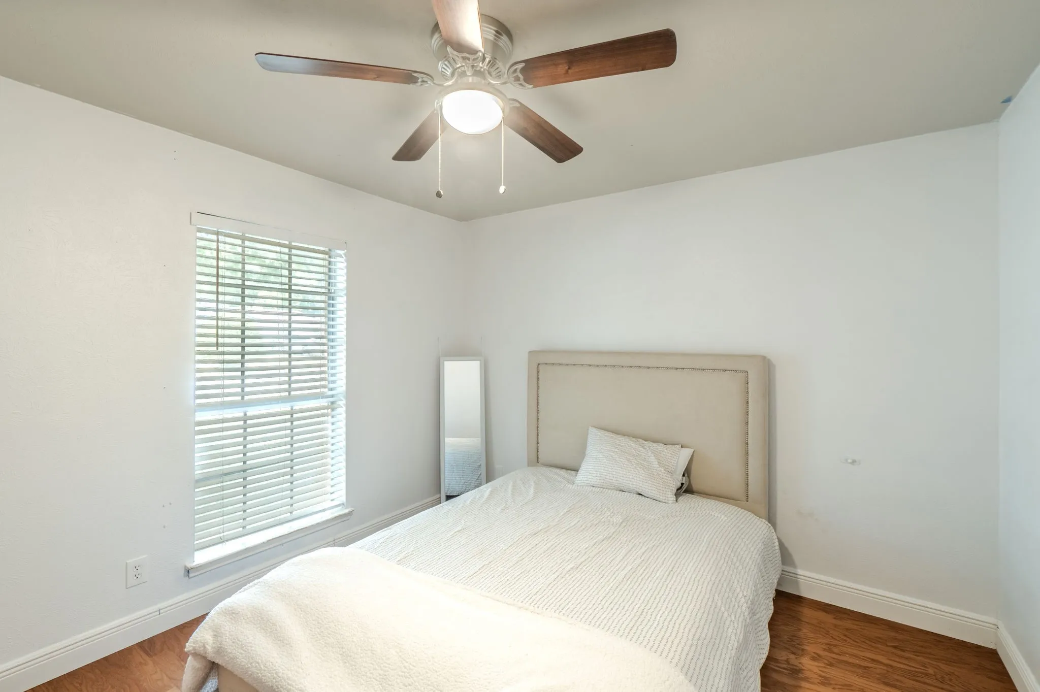 Wood-finish flooring, white walls, window with blinds, and a ceiling fan with integrated lighting
