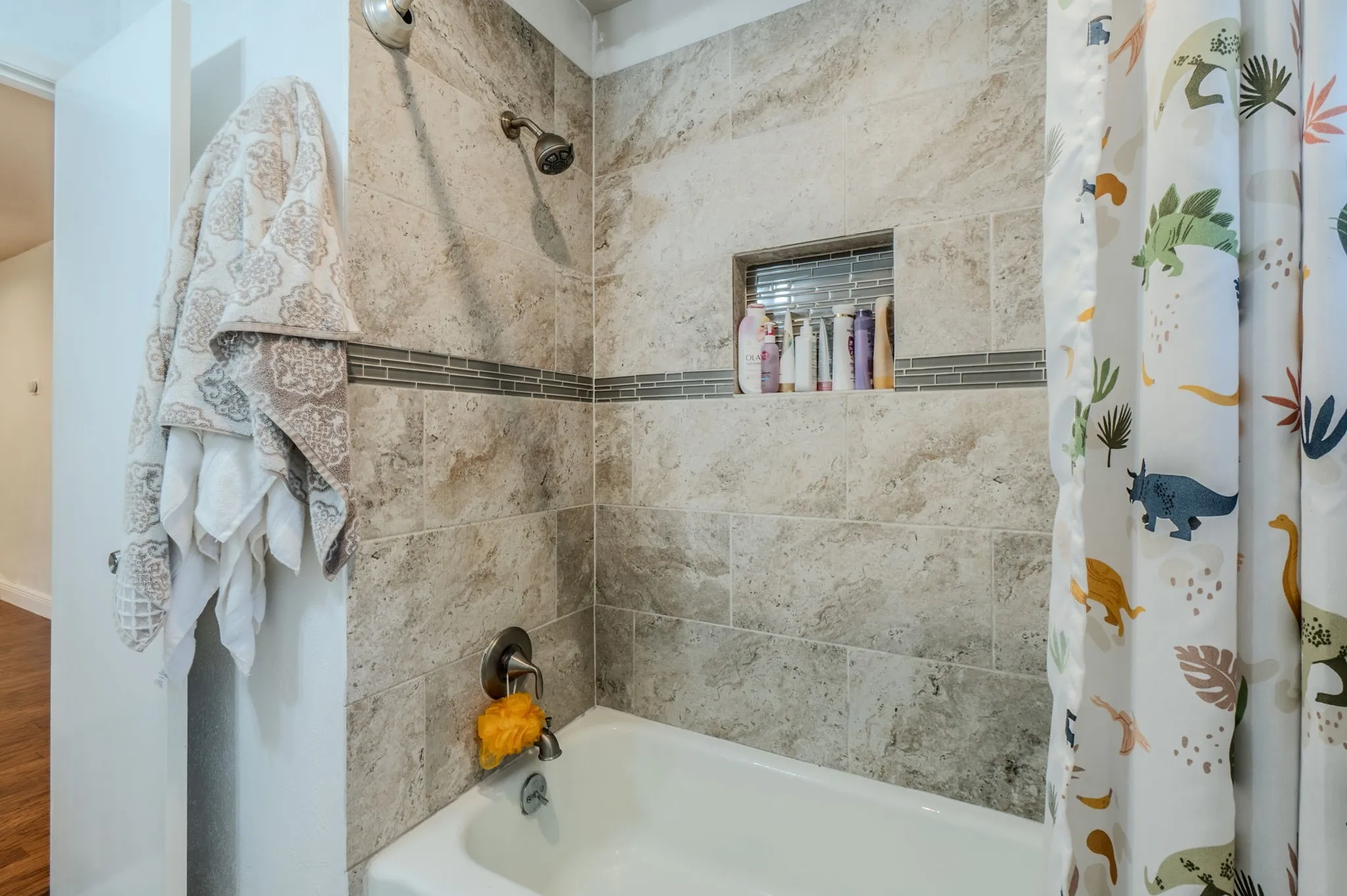 Bathtub featuring tile surround with decorative accent band and recessed niche