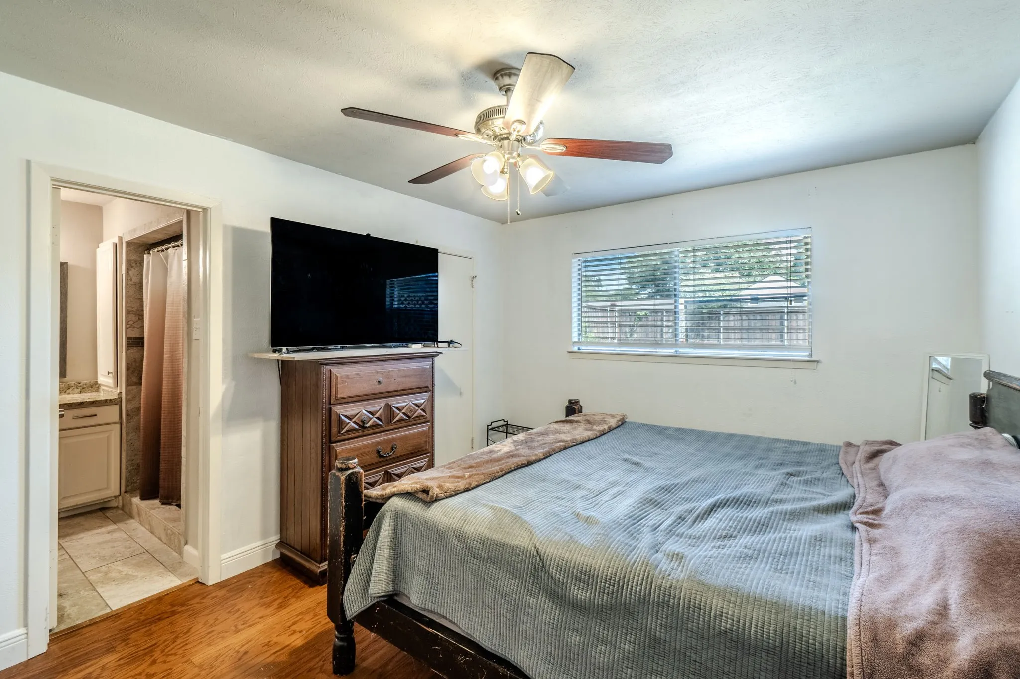 Wood-finish flooring, ceiling fan with integrated lighting, and a window with horizontal blinds