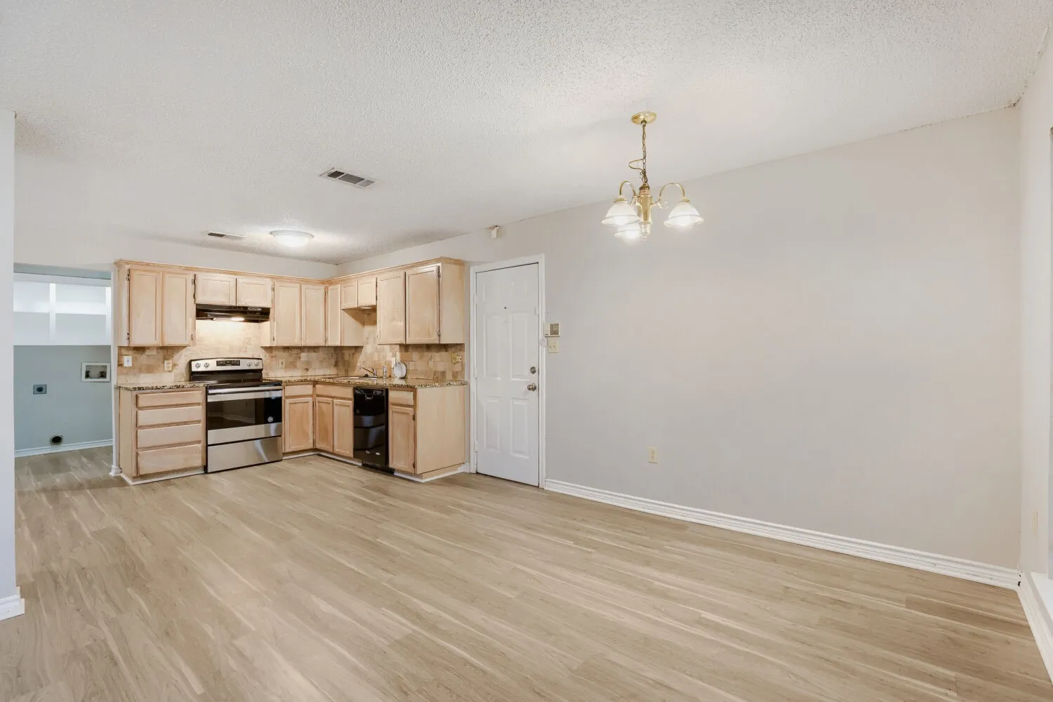 Open-concept living area with wood-finish flooring, a kitchen featuring stainless steel appliances, light-toned cabinetry, and a full-height backsplash