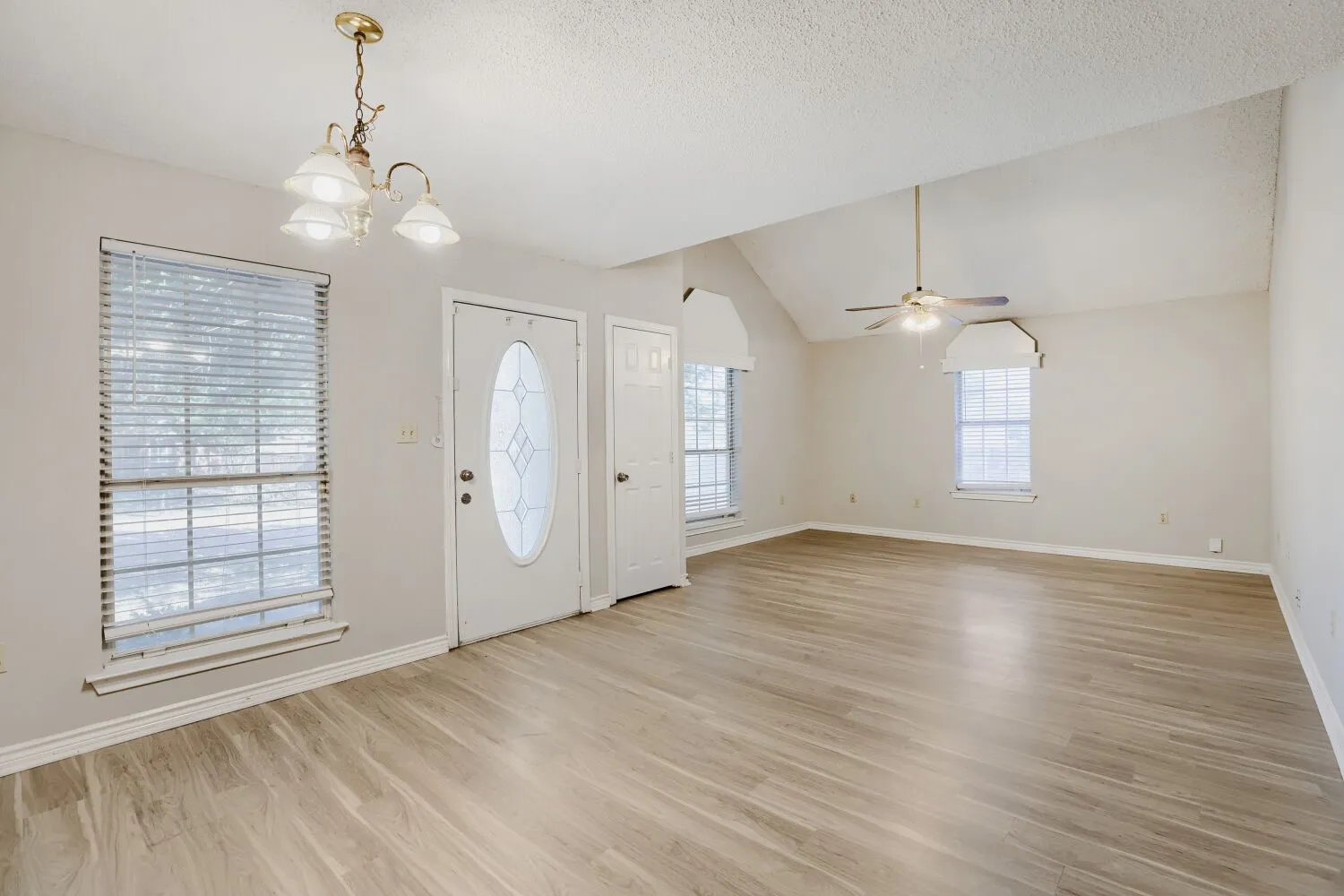 Vaulted ceiling, wood-finish flooring, ceiling fan, white paneled door with decorative glass insert, and a brass chandelier