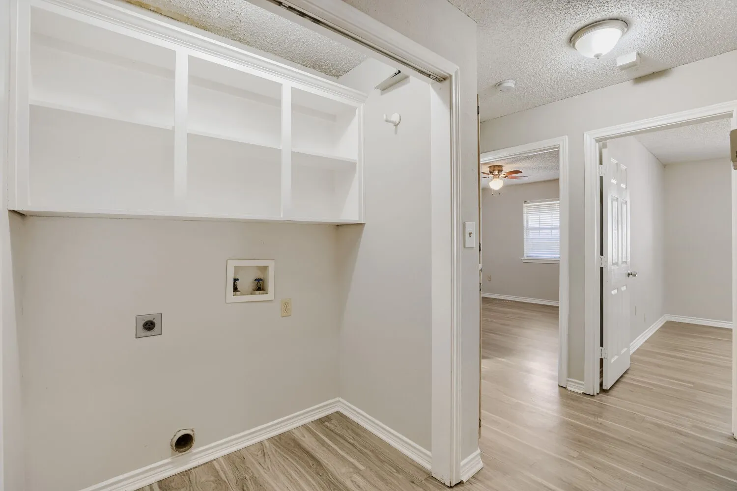 Laundry area with built-in open shelving and wood-finish flooring