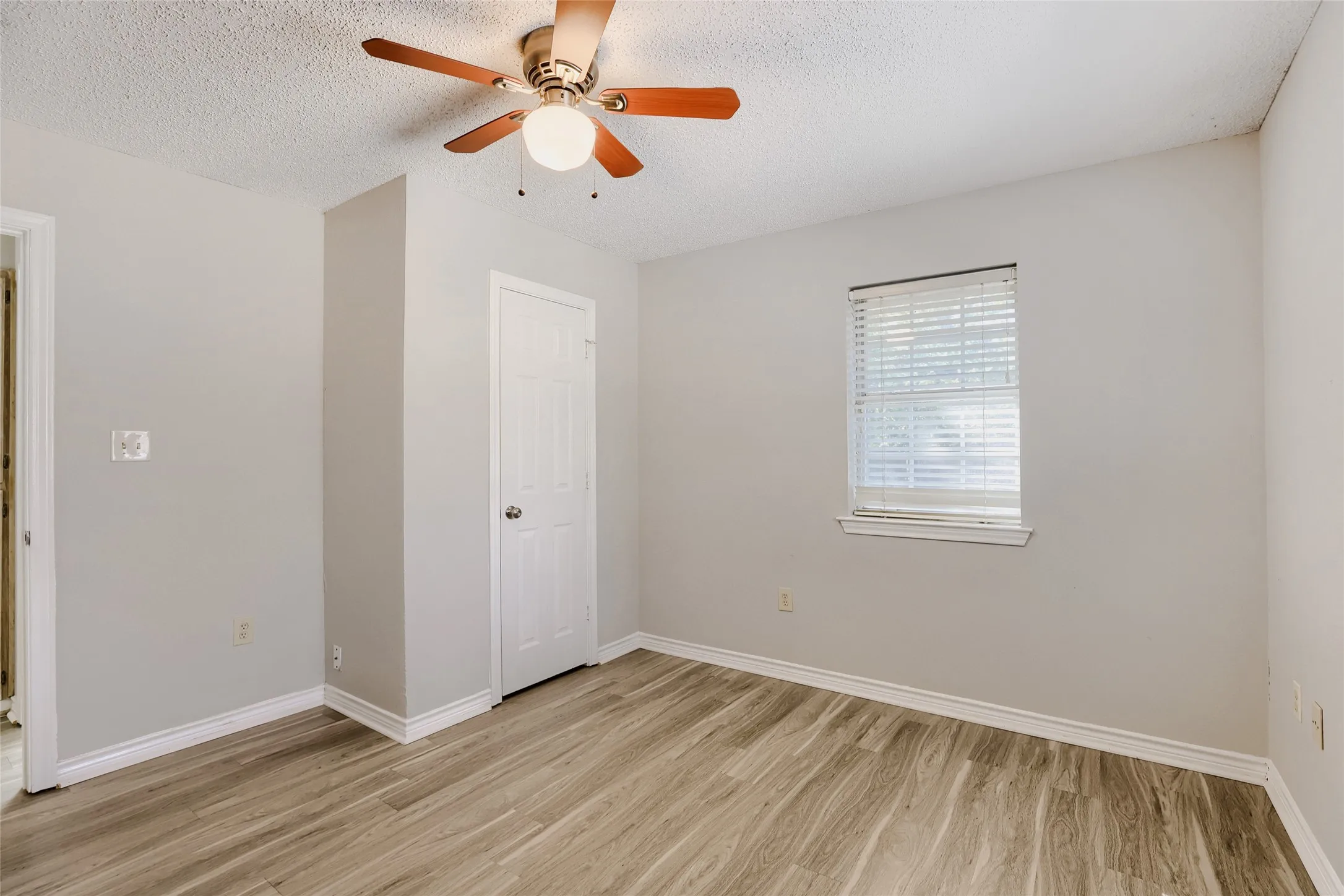 Wood-finish flooring, single window with blinds, ceiling fan with light fixture, and white trim