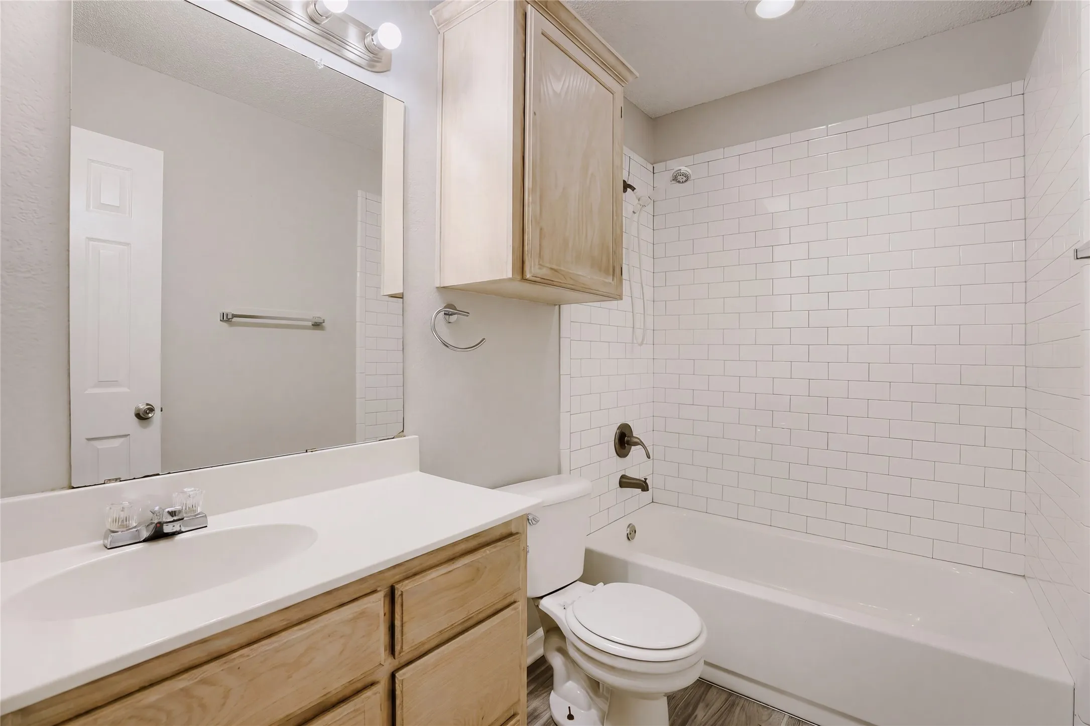 Bathroom featuring a white subway tile shower, built-in bathtub, light wood-finish vanity with a white countertop, and wood-finish flooring
