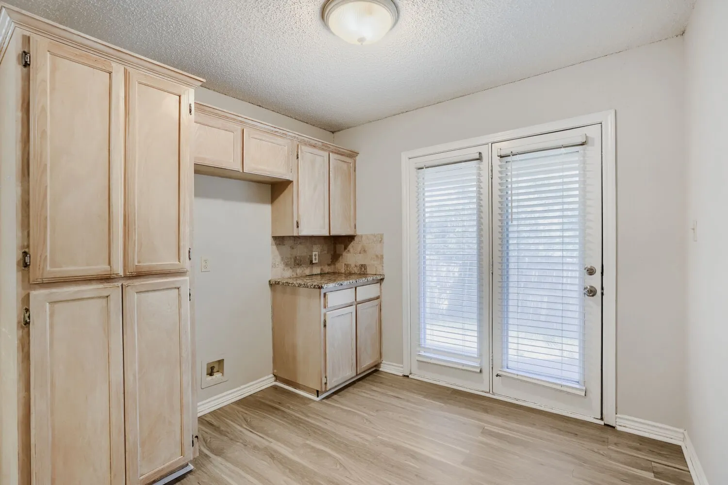 Wood-finish flooring, light wood cabinetry, stone backsplash, and white double patio doors